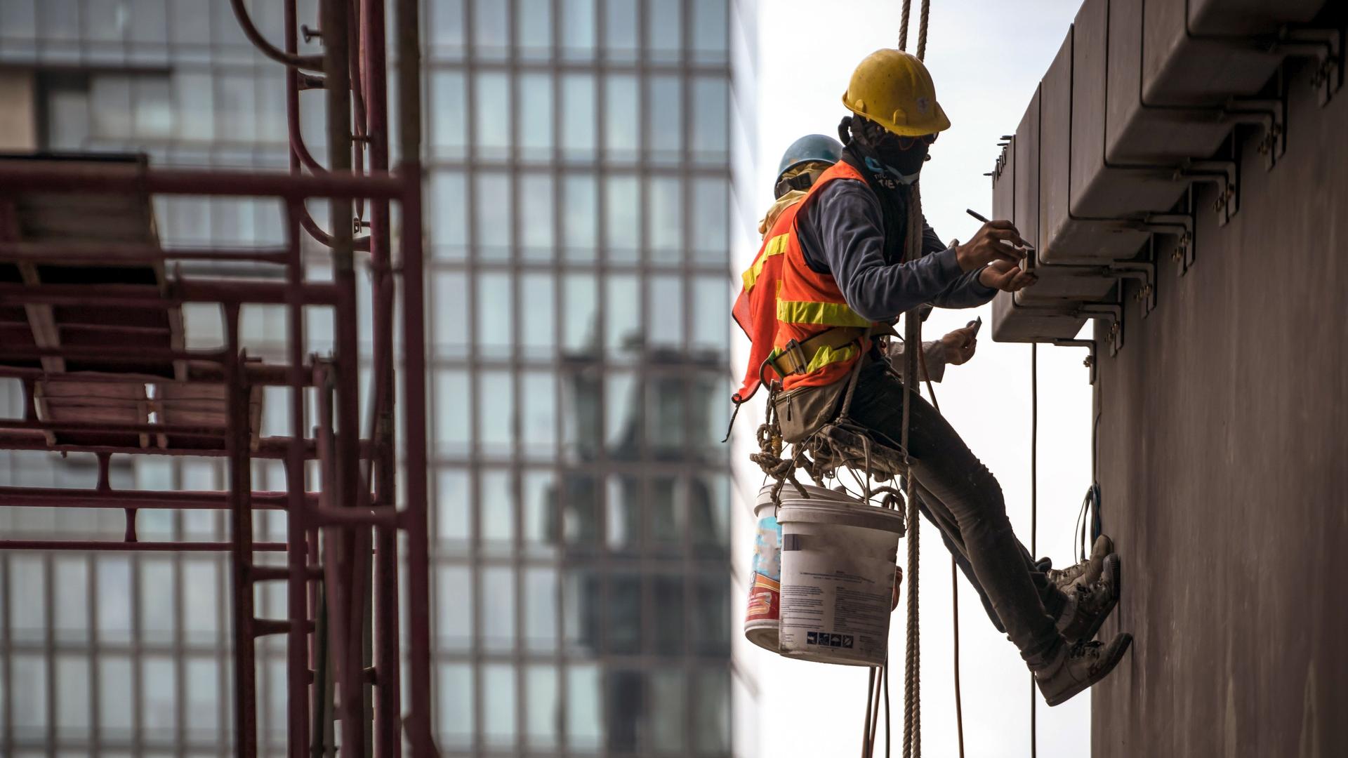 Bauarbeiter in Sicherheitsgurt hängt an Seil an einer Wand und arbeitet.