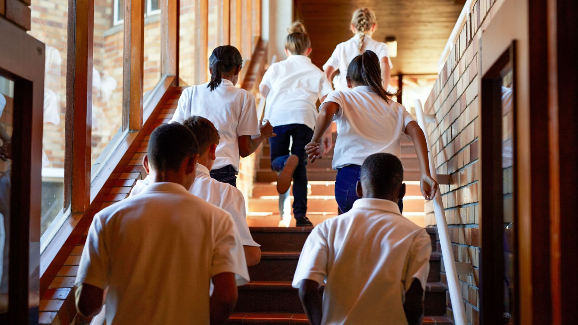 Blick von hinten auf Schulkinder, die in einem Schulgebäude die Treppen hochrennen