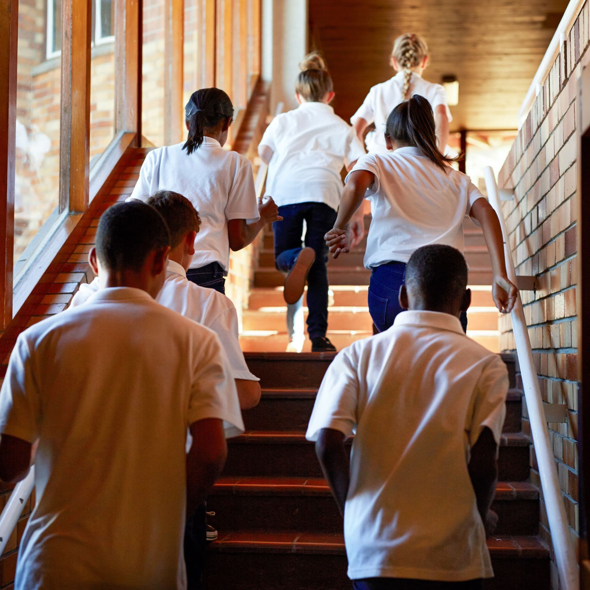 Blick von hinten auf Schulkinder, die in einem Schulgebäude die Treppen hochrennen