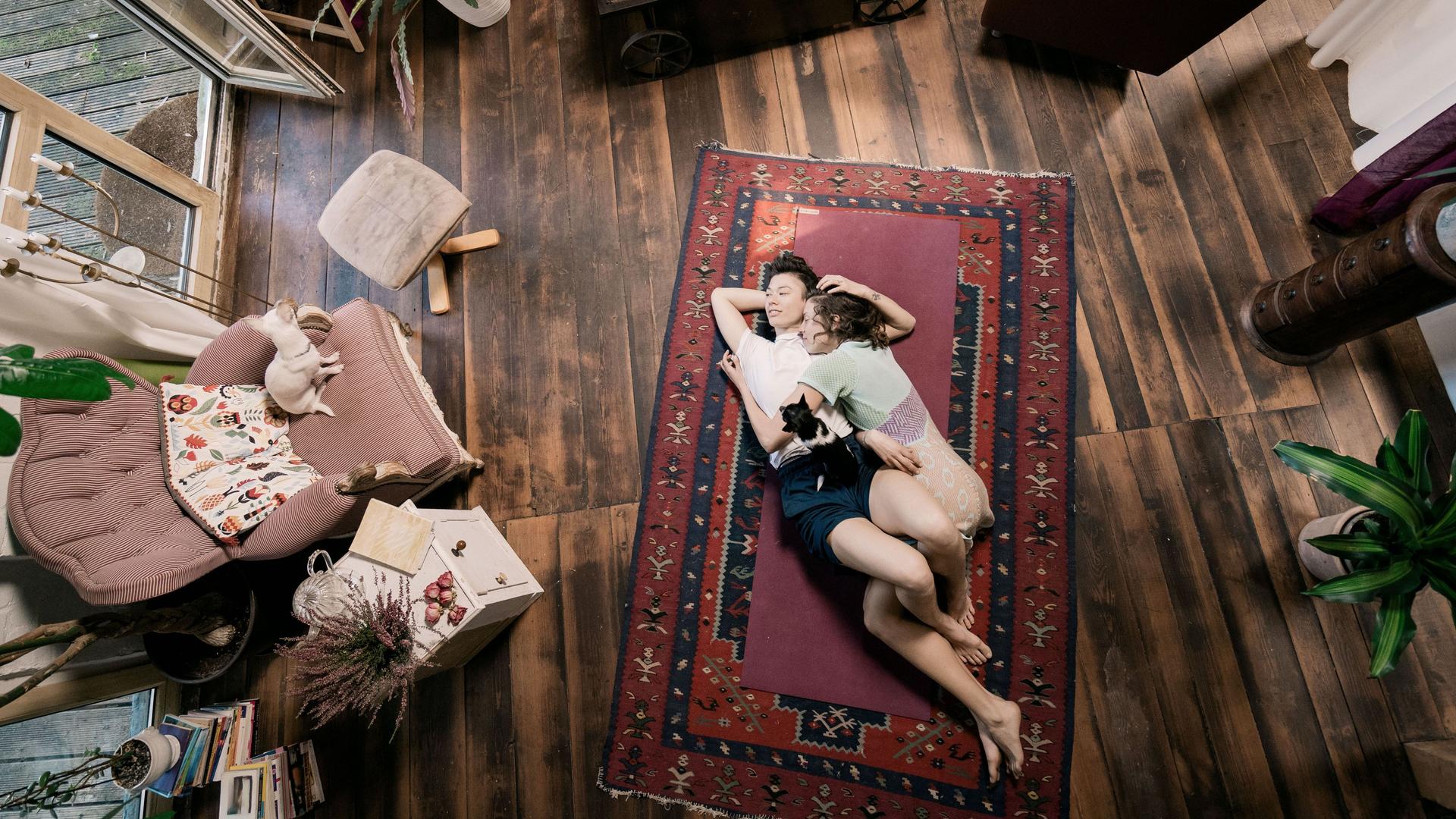 Blick von oben auf ein junges Paar, das auf dem Wohnzimmer auf einem Teppich am Boden liegt.