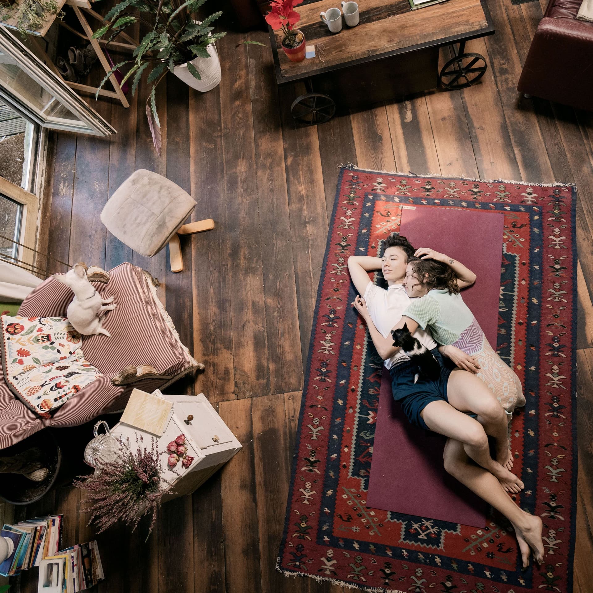 Blick von oben auf ein junges Paar, das auf dem Wohnzimmer auf einem Teppich am Boden liegt.