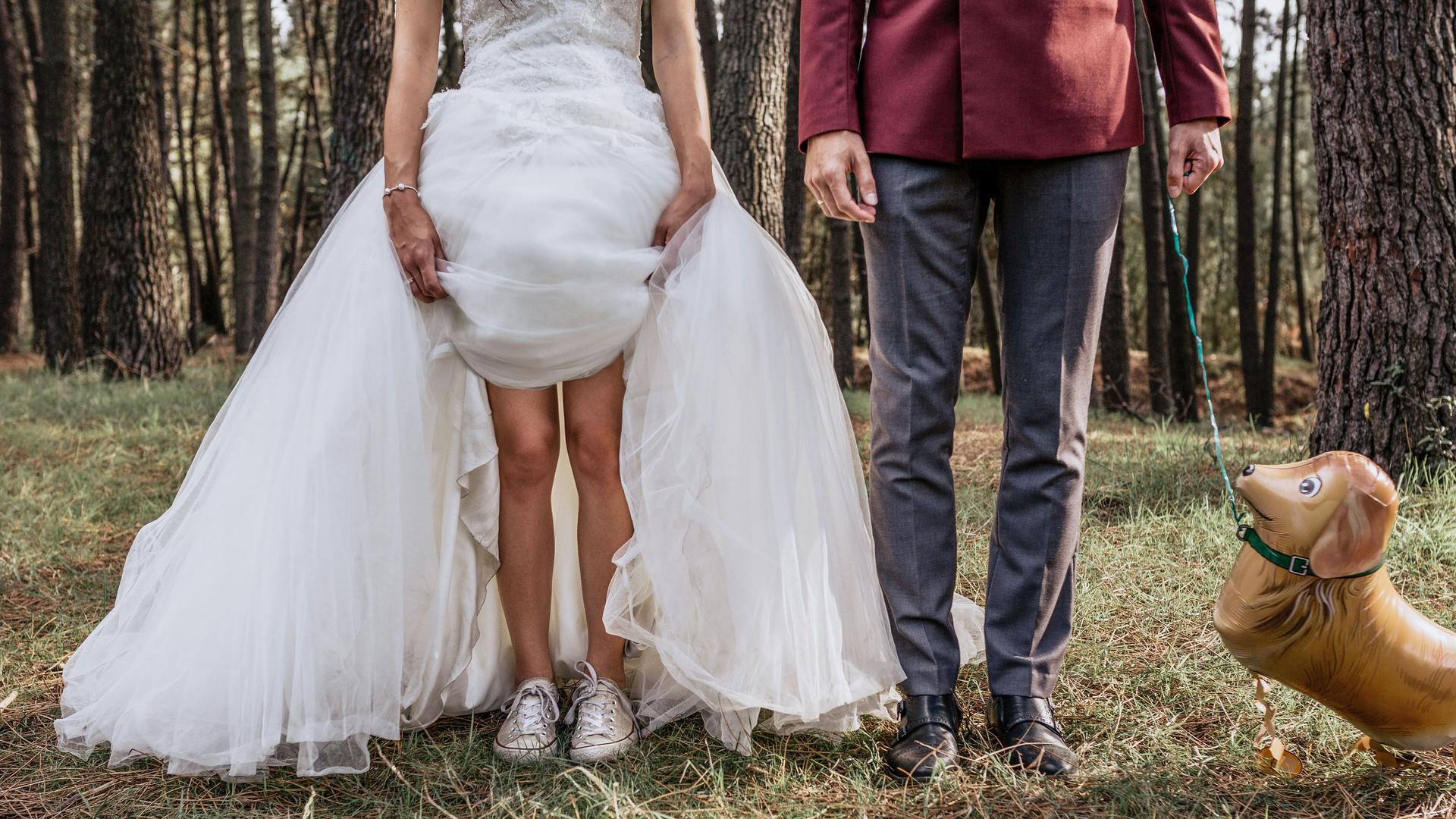 Brautpaar im Wald mit Luftballon Hund. Die Braut zieht ihr Hochzeitskleid über die Knie hoch.