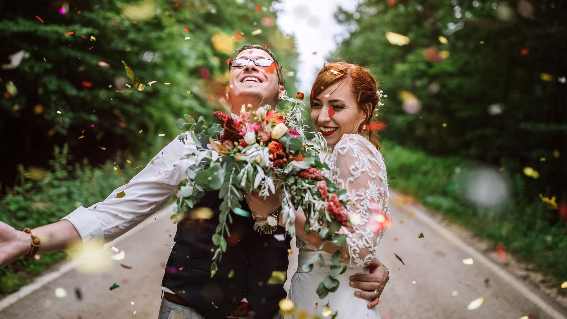 Junges Brautpaar feiert mit Konfetti und Brautstrauß