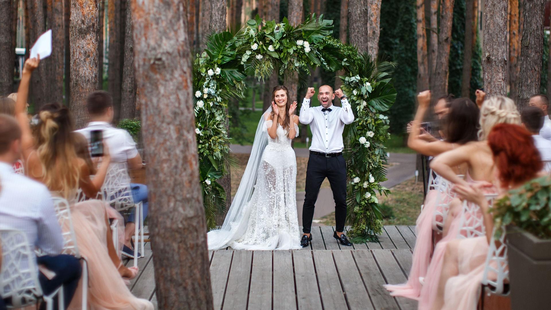 Brautpaar jubelt mit Hochzeitsgästen während ihrer Trauung im Wald