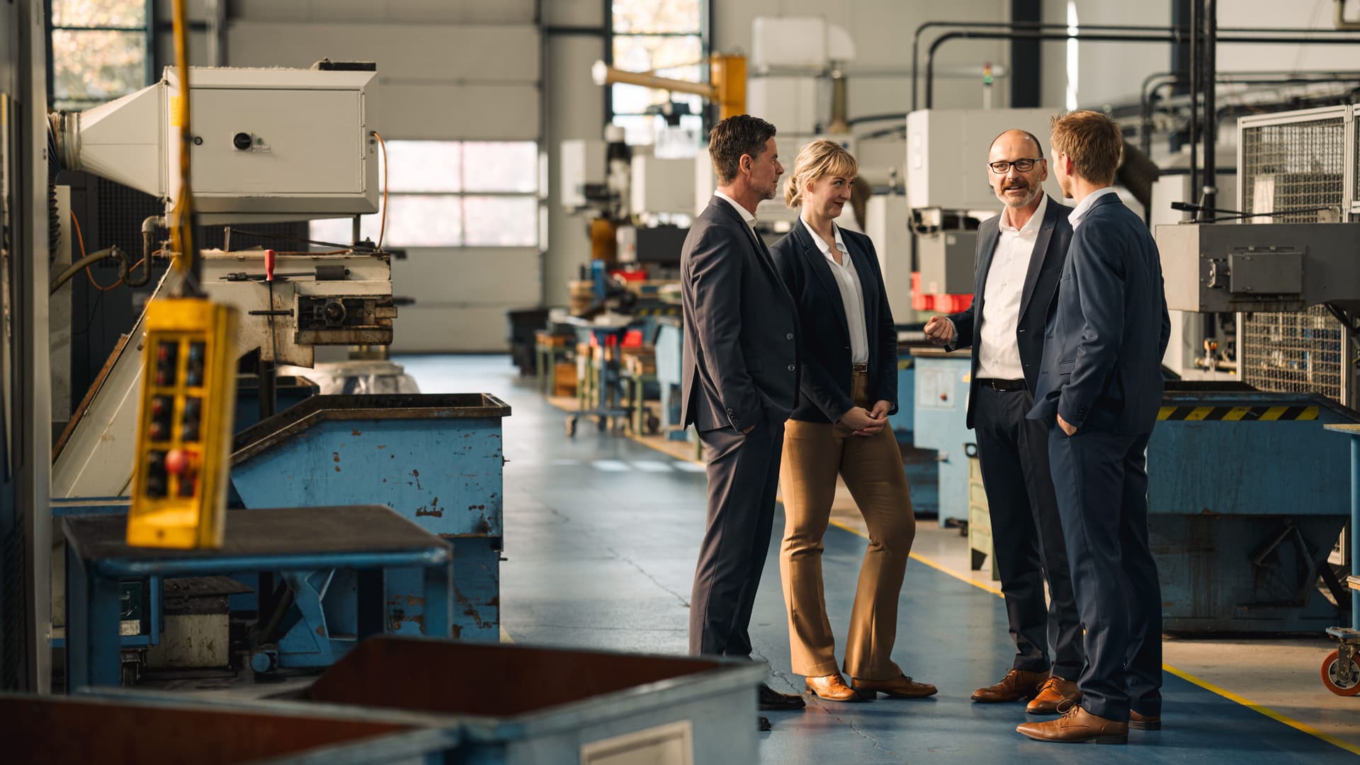 Eine Frau und drei Männer stehen zusammen bei einem Meeting in einer Fabrik.