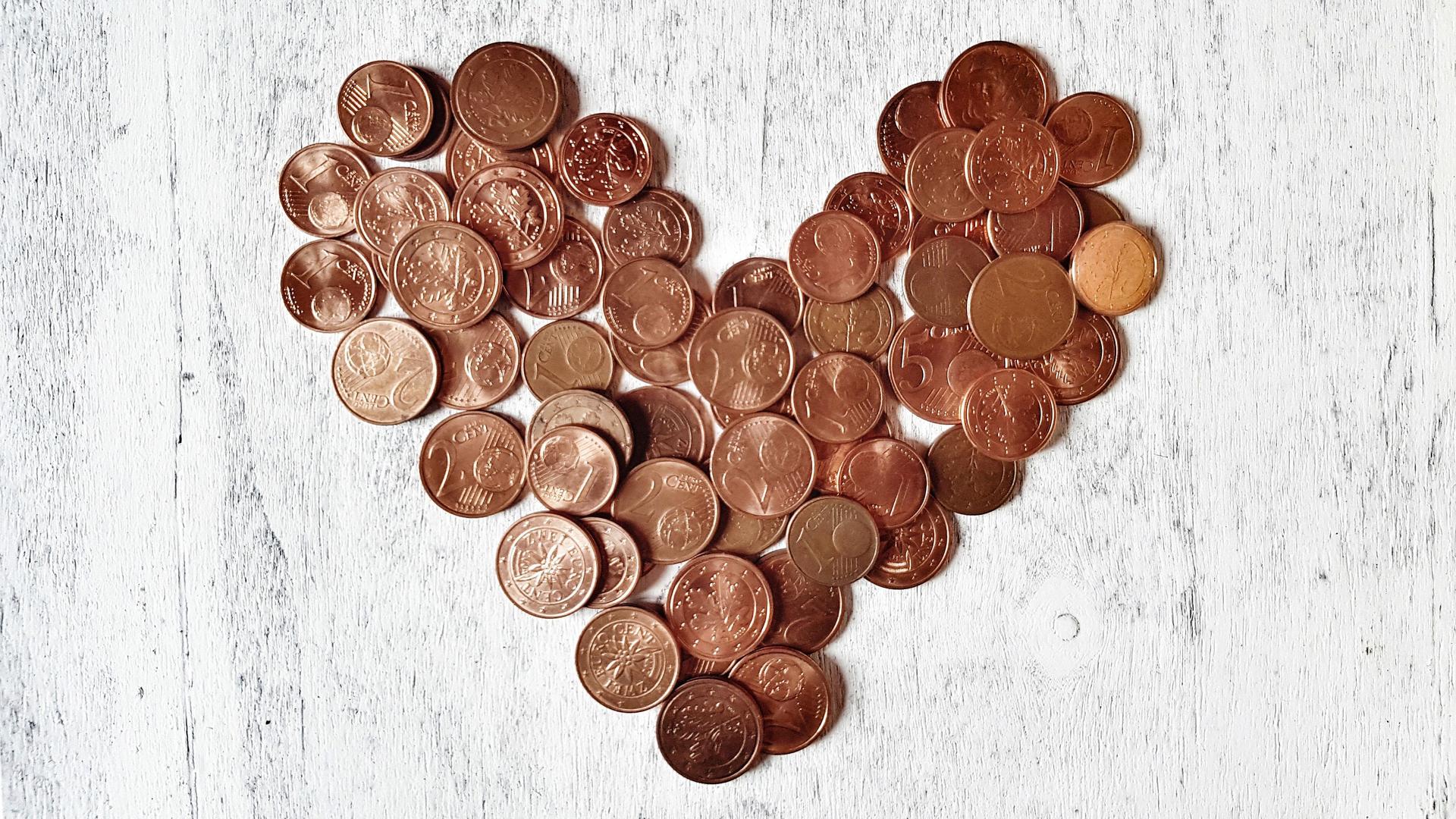 Nahaufnahme von Cent-Münzen in Herzform auf einem hellen Holzuntergrund angeordnet.