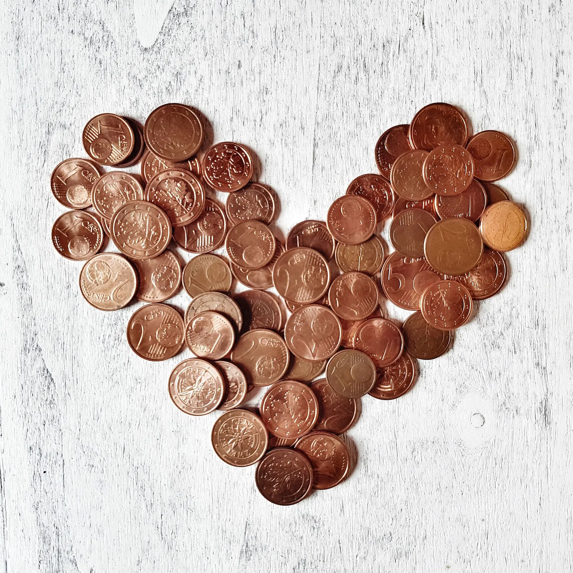 Nahaufnahme von Cent-Münzen in Herzform auf einem hellen Holzuntergrund angeordnet.