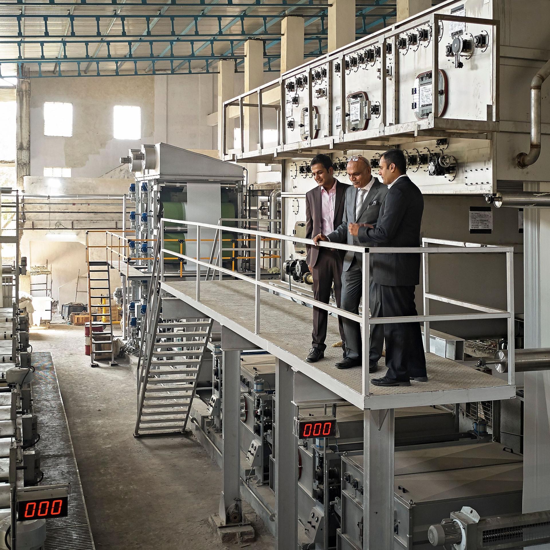Drei Männer im Anzug, die auf einer erhöhten Plattform steht und das Fabriklayout in der Färberei und Druckerei in Mumbai studieren.