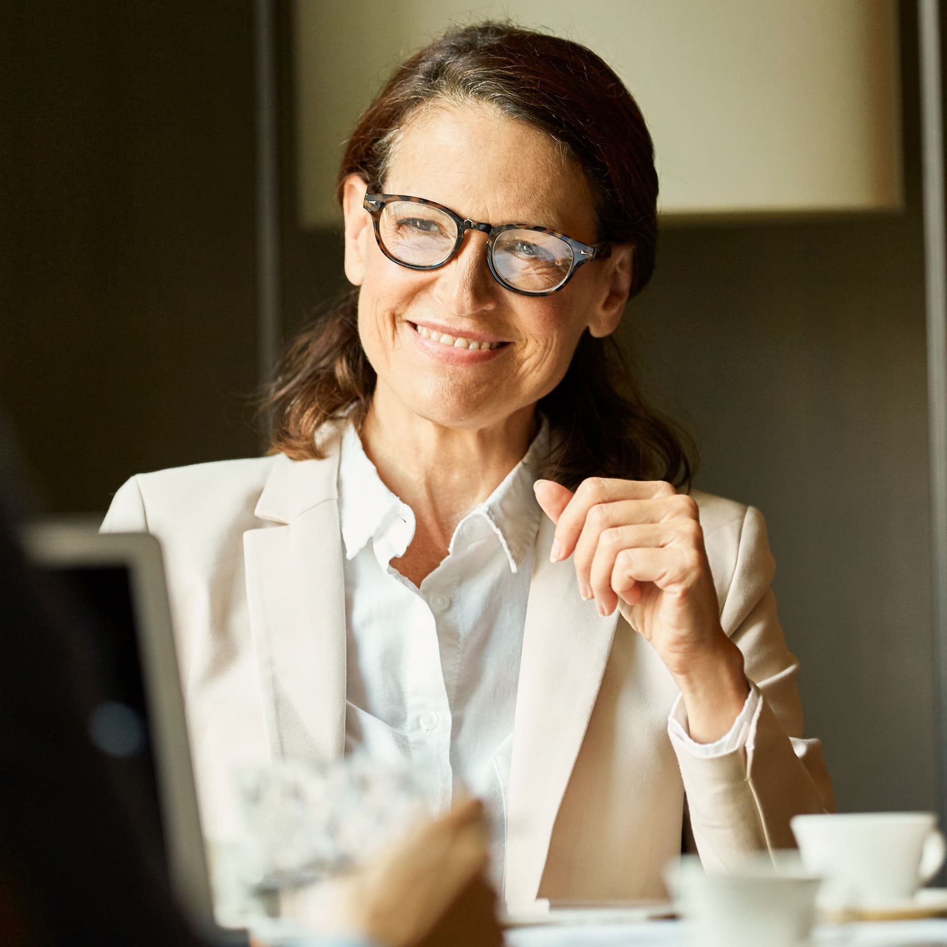 Frau in Business-Kleidung blickt lächelnd während einer Besprechung an einem Tisch zu ihrem Gegenüber.