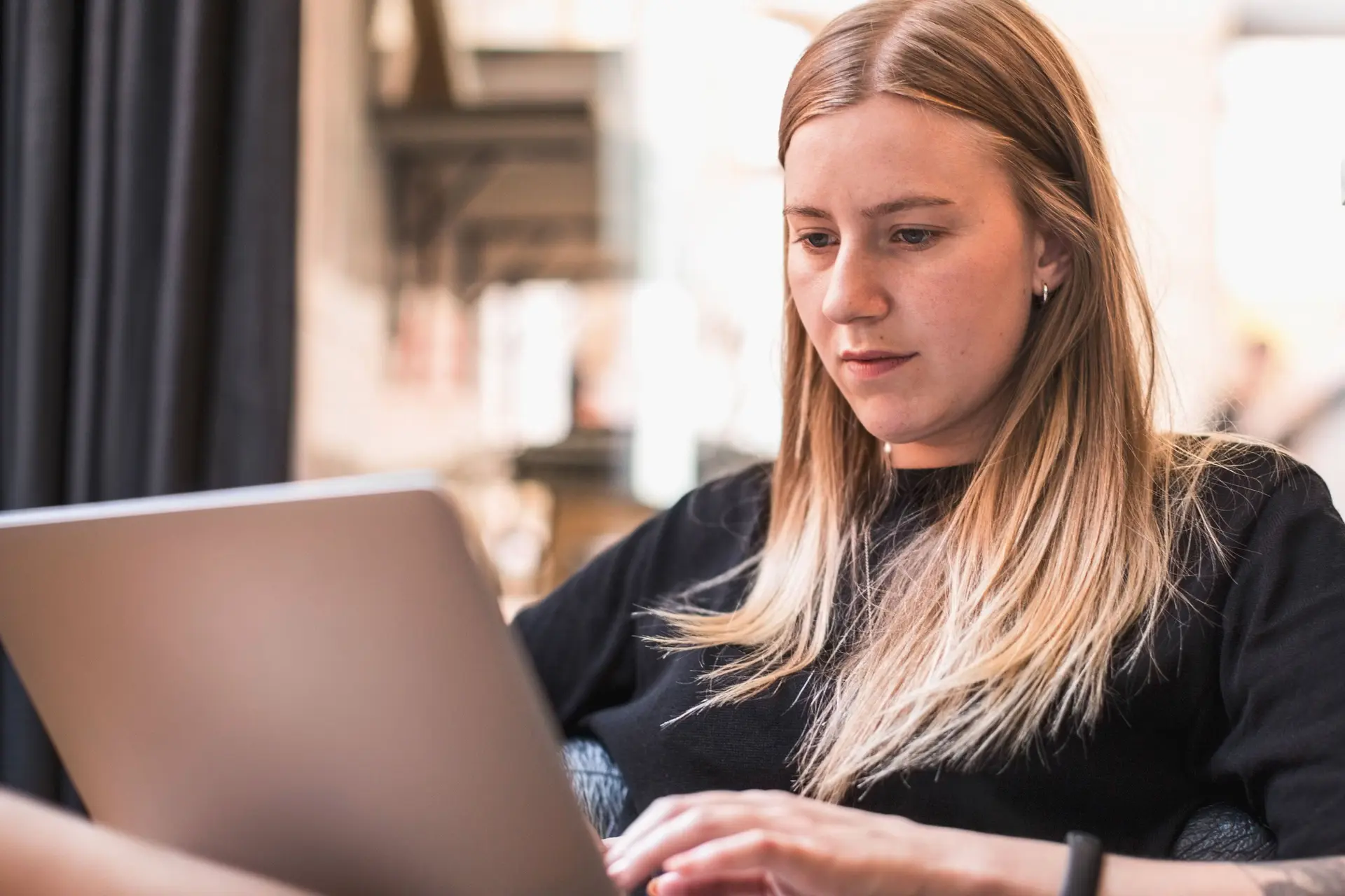 Junge Frau sitzt mit einem Laptop auf dem Schoss und schreibt