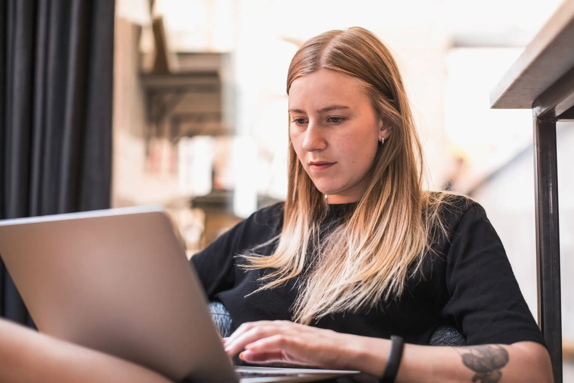 Junge Frau sitzt mit einem Laptop auf dem Schoss und schreibt