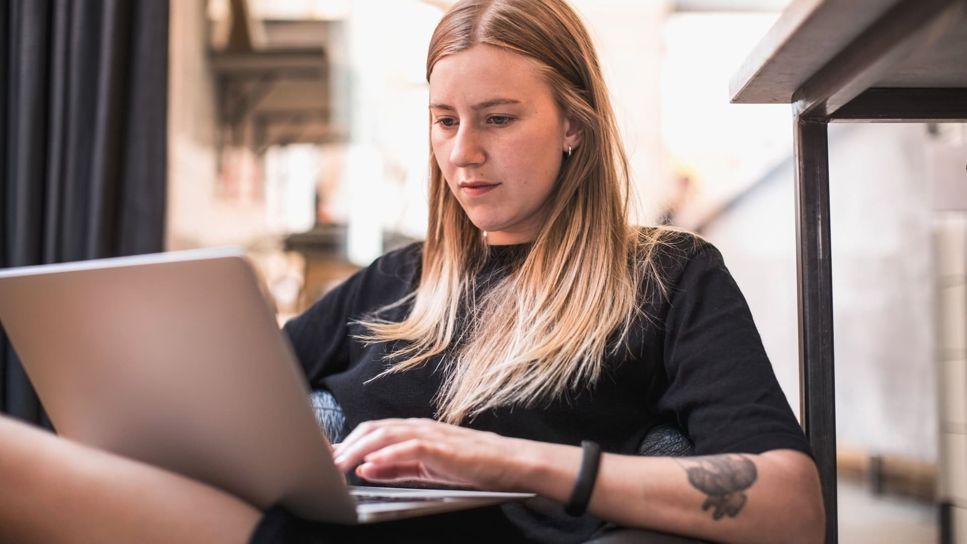 Junge Frau sitzt mit einem Laptop auf dem Schoß und schreibt