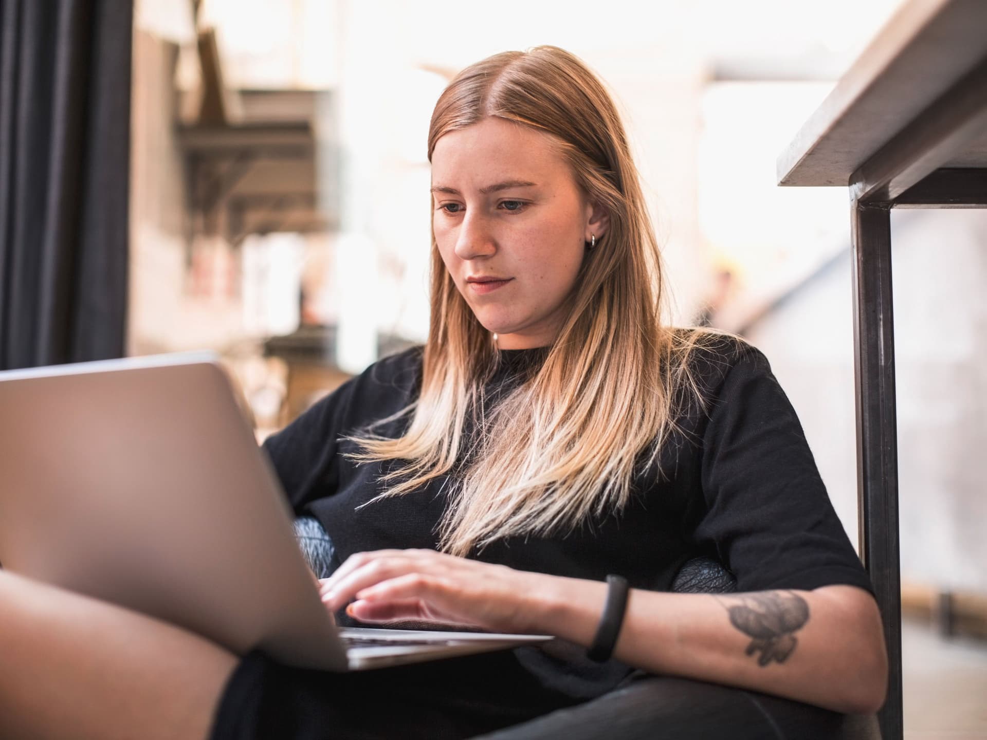 Junge Frau sitzt mit einem Laptop auf dem Schoß und schreibt