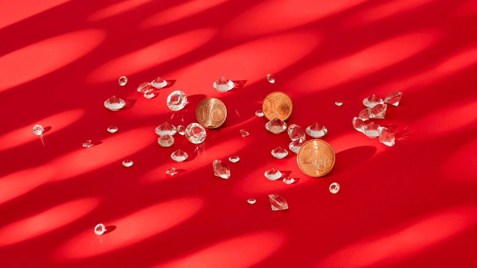 Diamanten und Kupfegeld liegen auf einem roten Untergrund. Sie werden von einem Muster aus runden Lichtflecken beleuchtet.