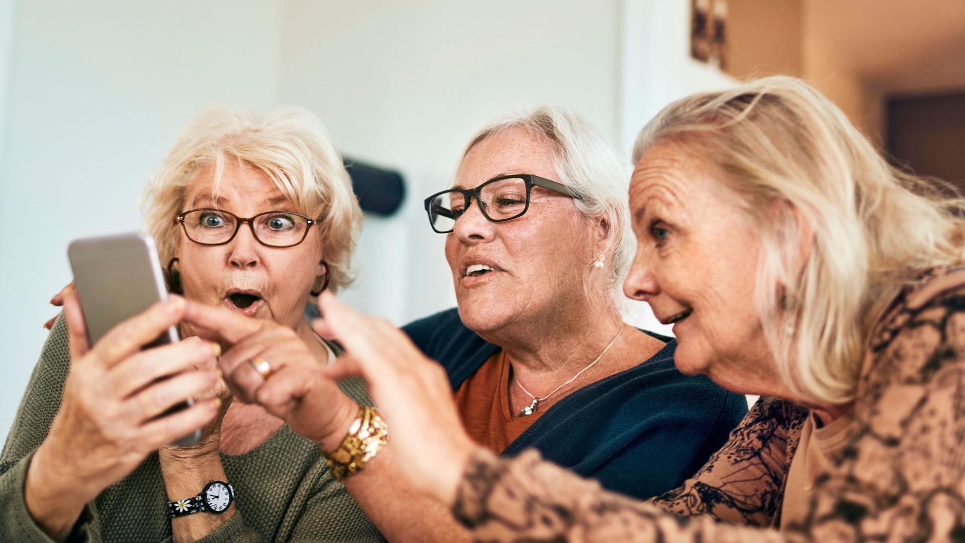 Drei ältere Damen beim Kaffee Kuchen amüsieren sich mit Handy