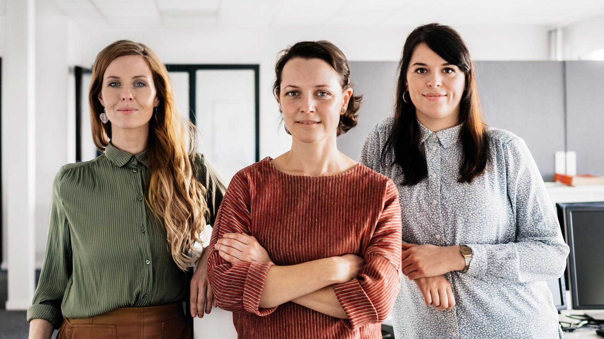 Drei Frauen stehen in einem Büro. Im Hintergrund sind Computer.