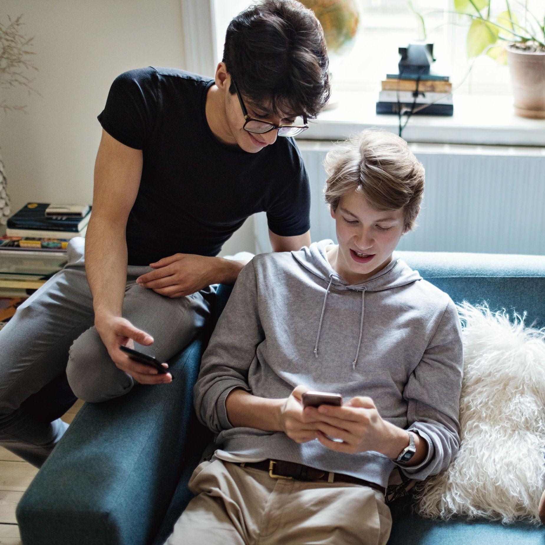 drei Teenager Jungen schauen auf einem Sofa zuhause auf Smartphones 