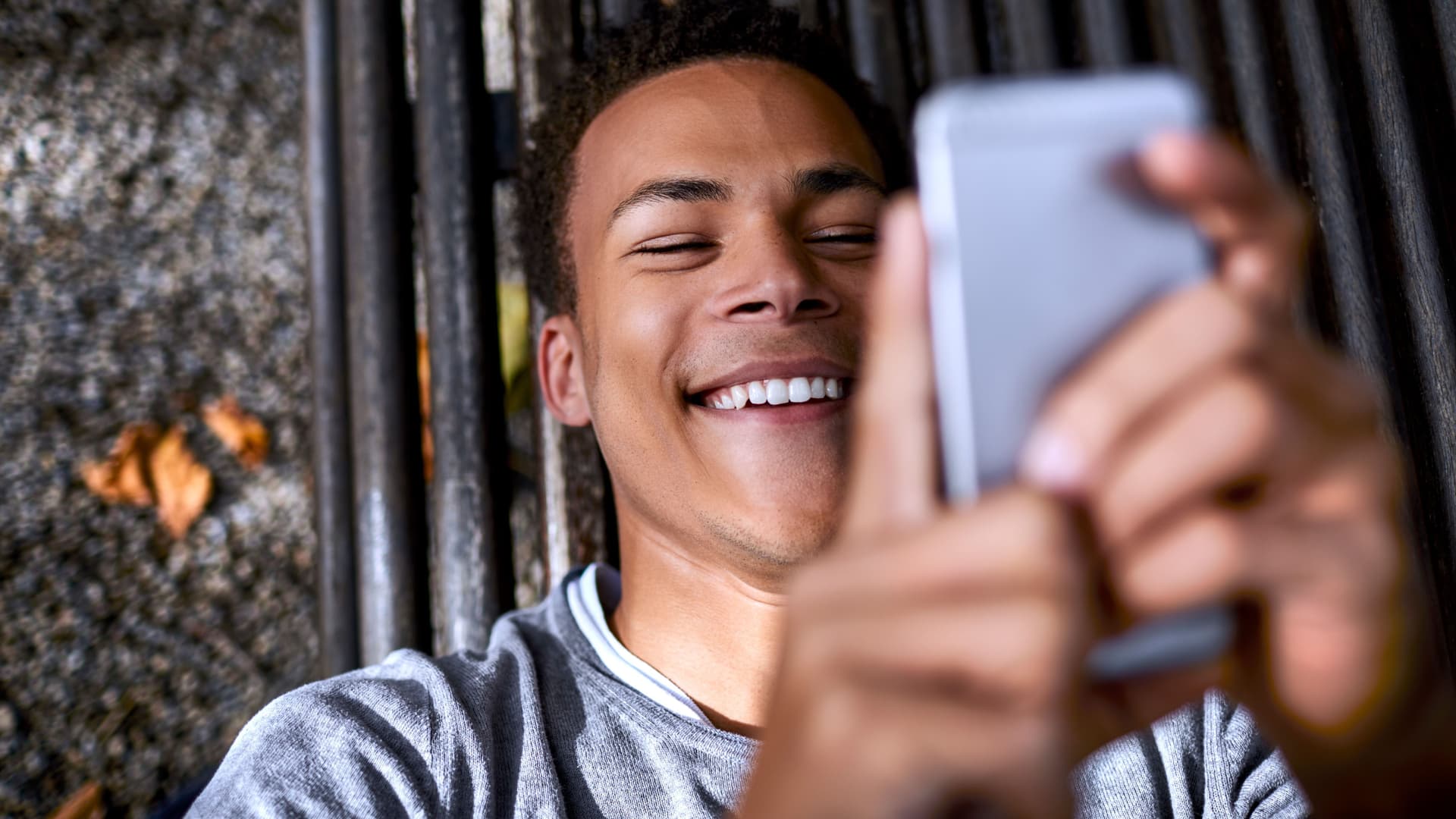 Ein Jugendlicher liegt lächenld auf einer Bank und schaut auf sein Handy.
