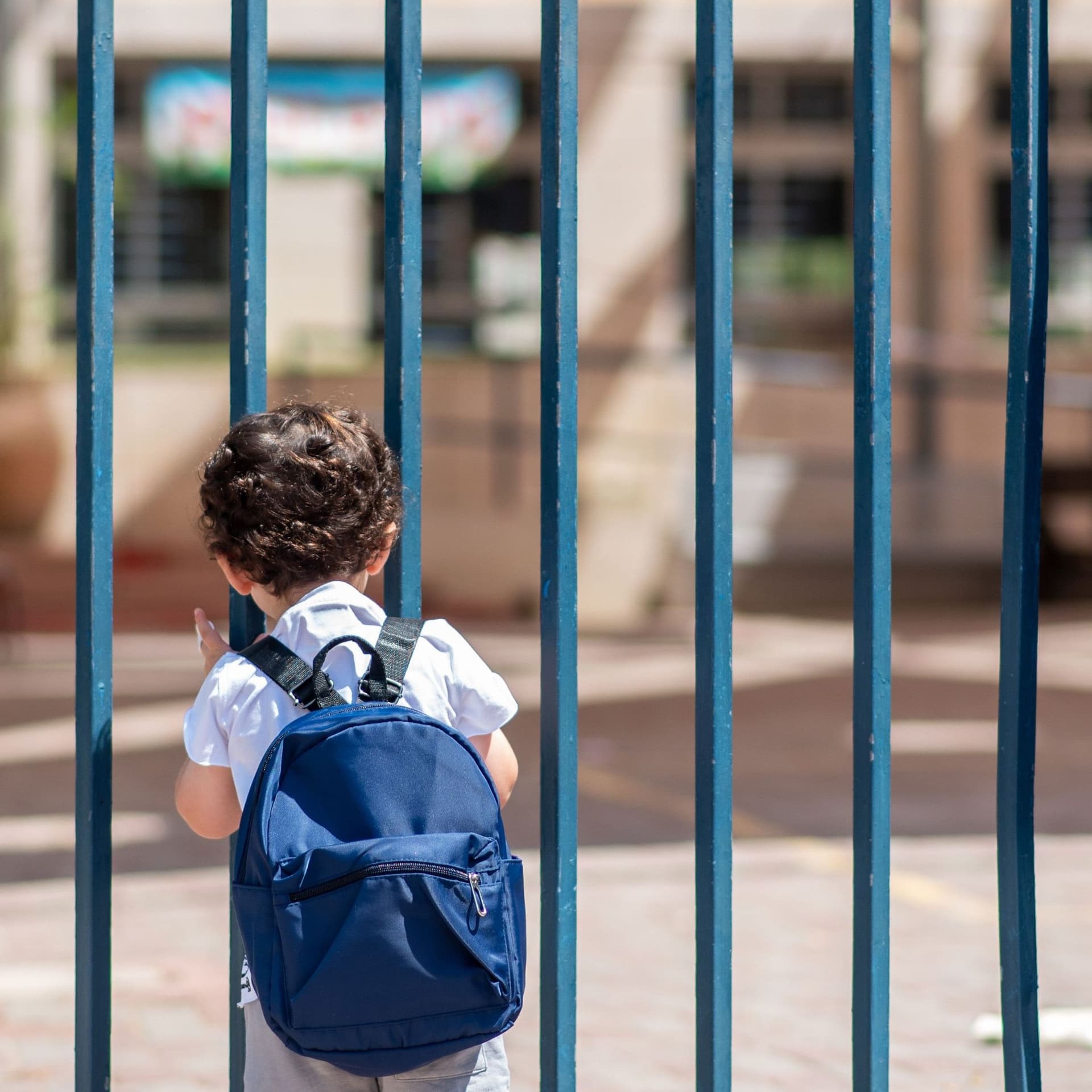 Ein kleiner Junge steht vor einem verschlossenen Kita-Tor. Er schaut in den Hof.