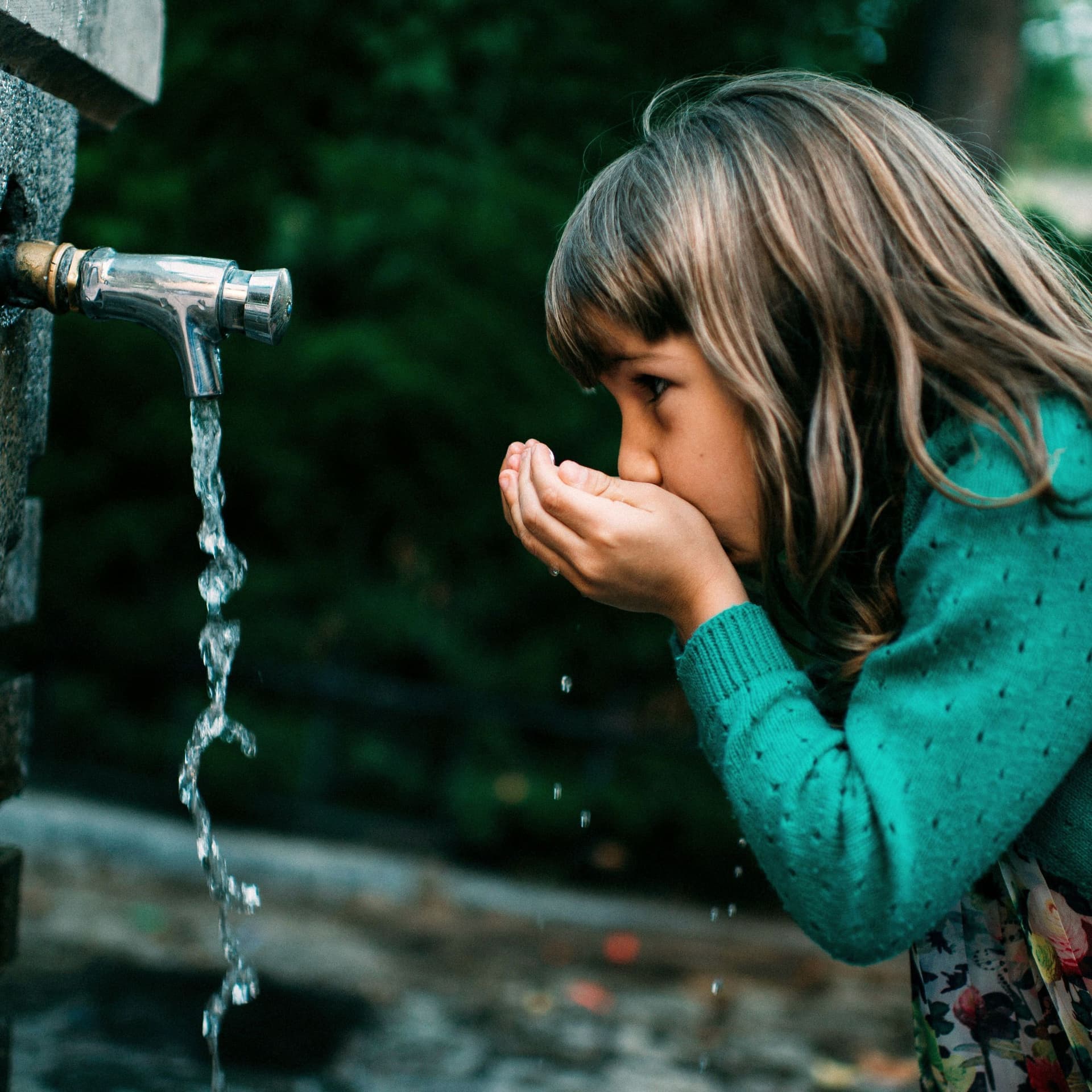 Ein Mädchen trinkt Wasser aus einem Trinkbrunnen in der Natur