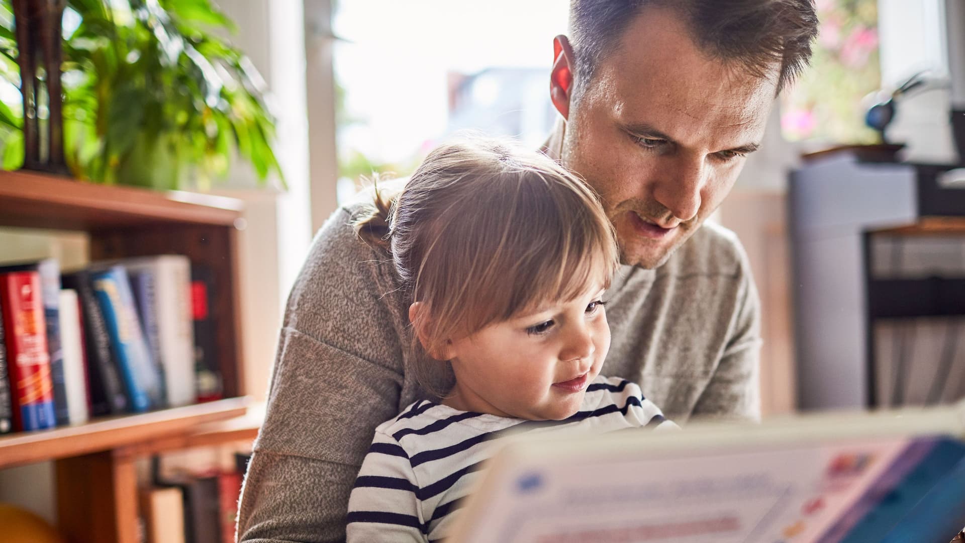 Ein Mann liest einem Kind in einem Wohnzimmer aus einem Buch vor