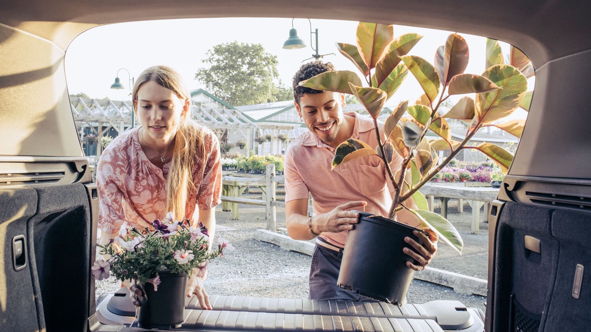 Eine Frau und ein Mann kaufen Pflanzen ein. Sie laden sie ins Auto.