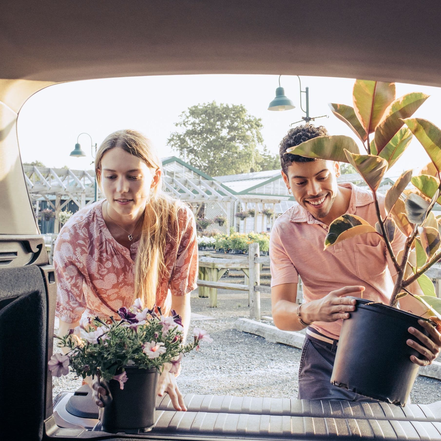 Eine Frau und ein Mann kaufen Pflanzen ein. Sie laden sie ins Auto.
