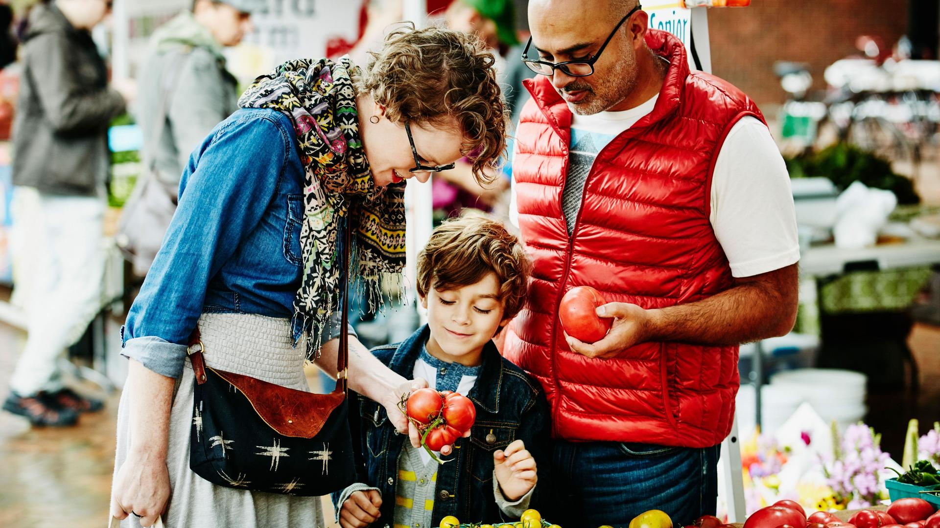 Eine Familie geht auf einem Wochenmarkt einkaufen. Sie schauen sich die Tomaten an.