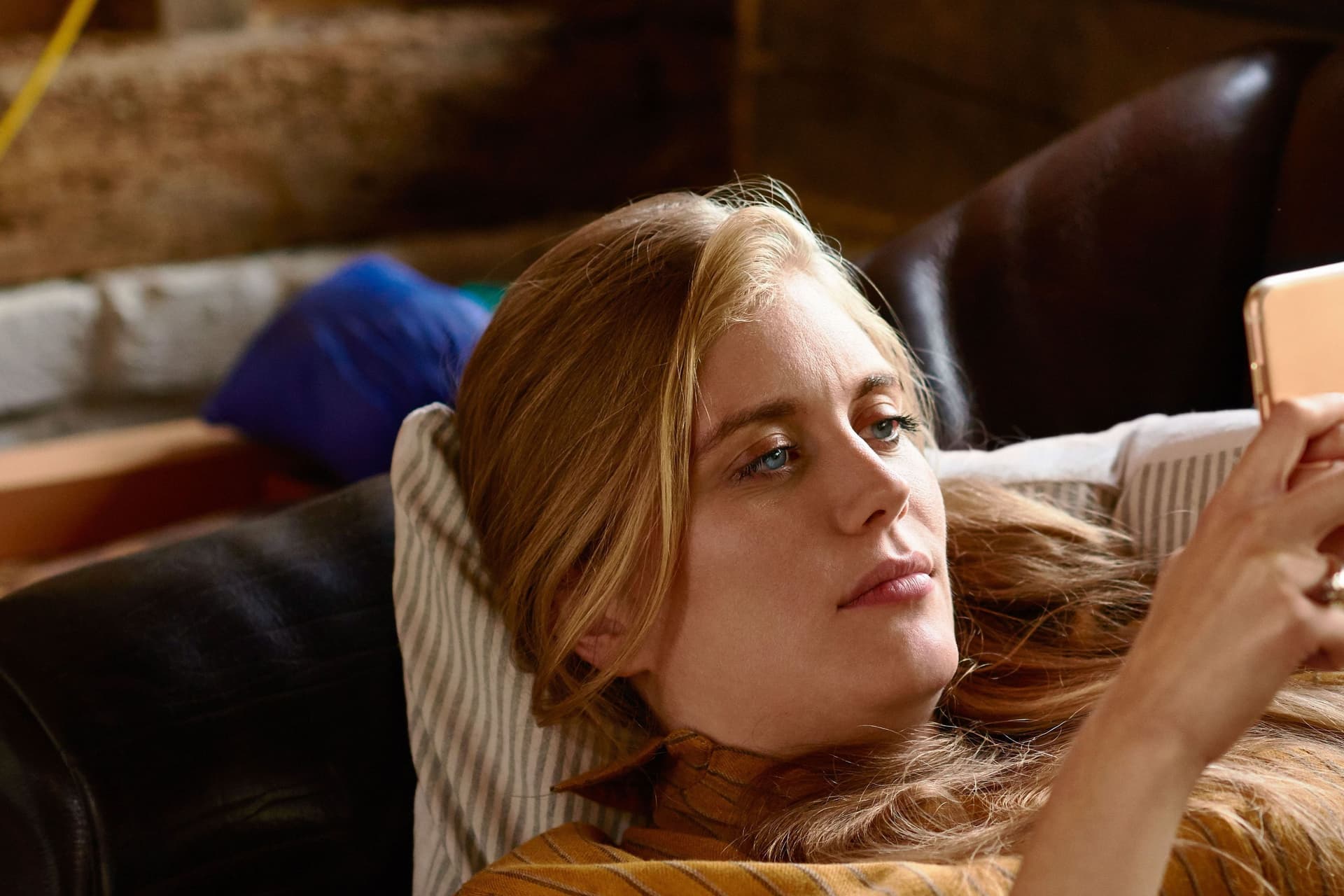 Eine blonde Frau liegt mit ihrem Handy in der Hand auf einem Sofa.