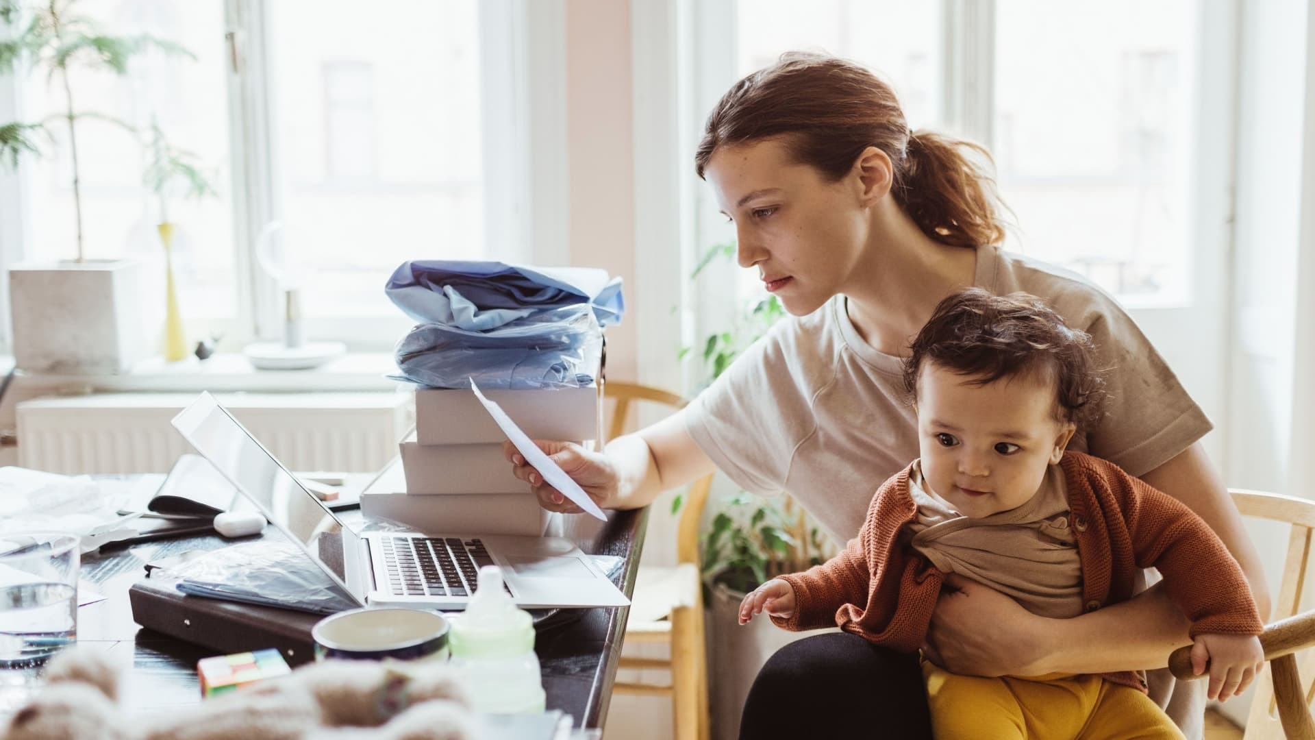 Eine junge Frau mit Kind auf dem Schoss sitzt am Schreibtisch,. Sie schaut auf einen Bescheid.