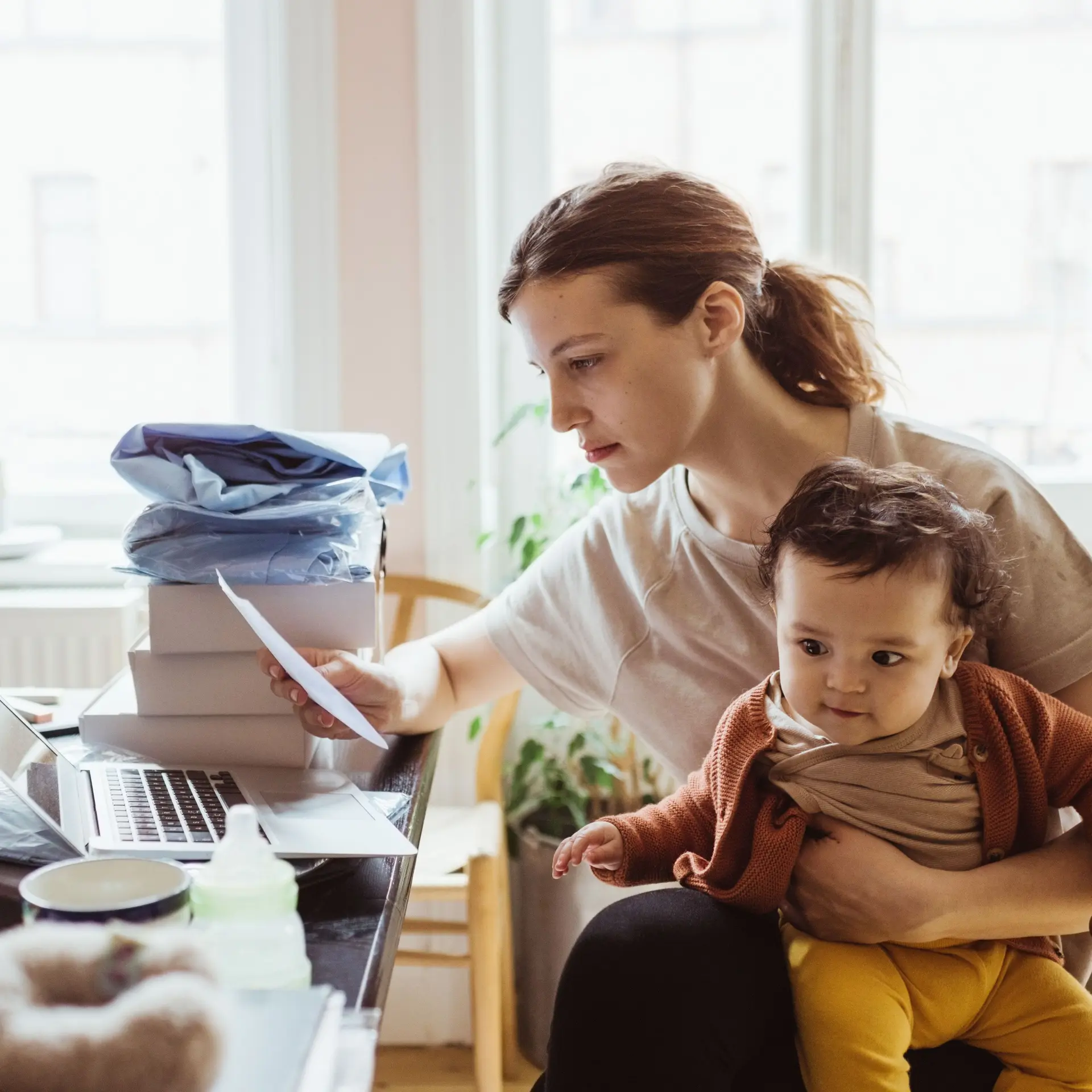 Eine junge Frau mit Kind auf dem Schoss sitzt am Schreibtisch,. Sie schaut auf einen Bescheid.