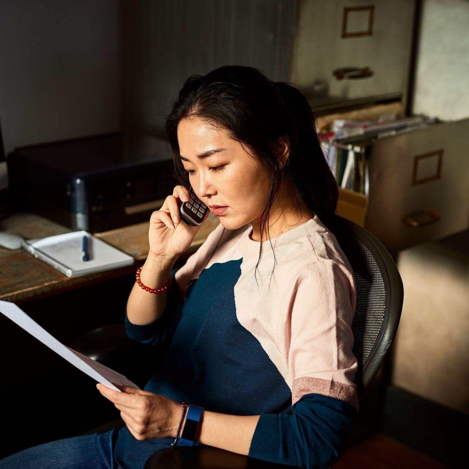 Eine Frau sitzt vor einem Schreibtisch schaut sorgenvoll auf eine Rechnung und telefoniert