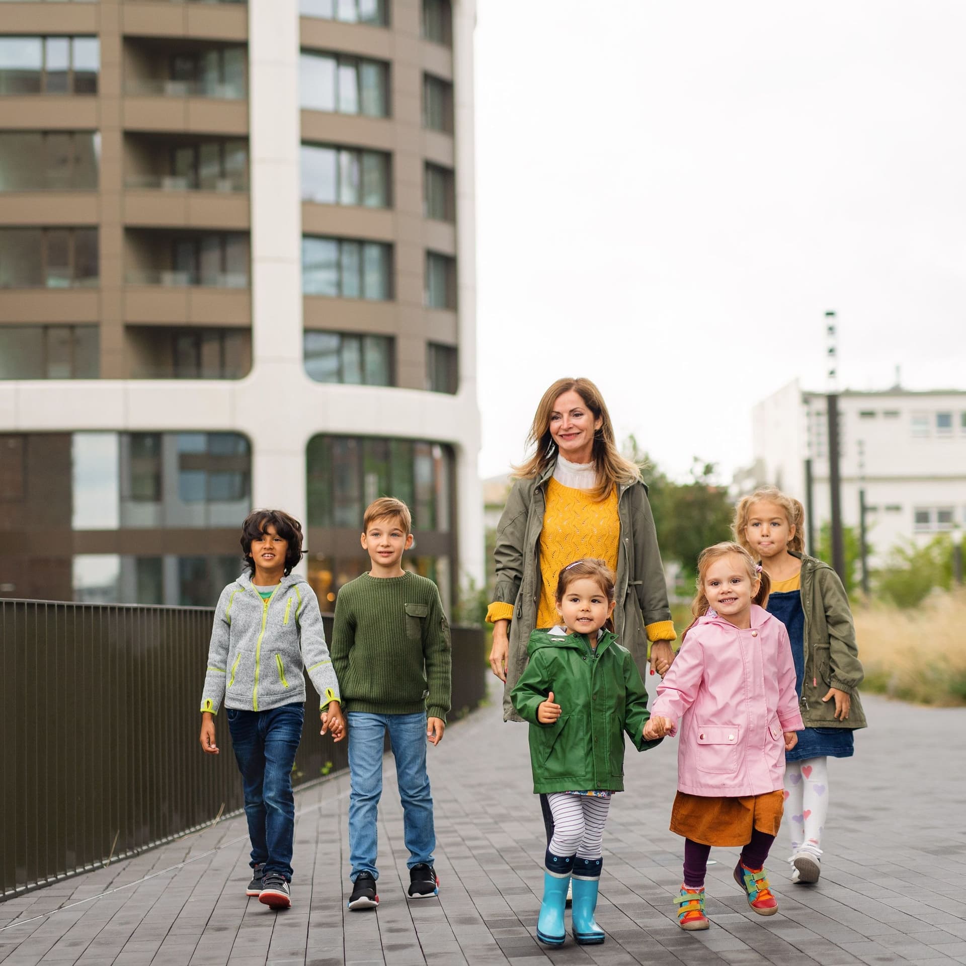 Eine Erzieherin läuft mit einer Gruppe von 5 Kindern durch eine urbane Landschaft