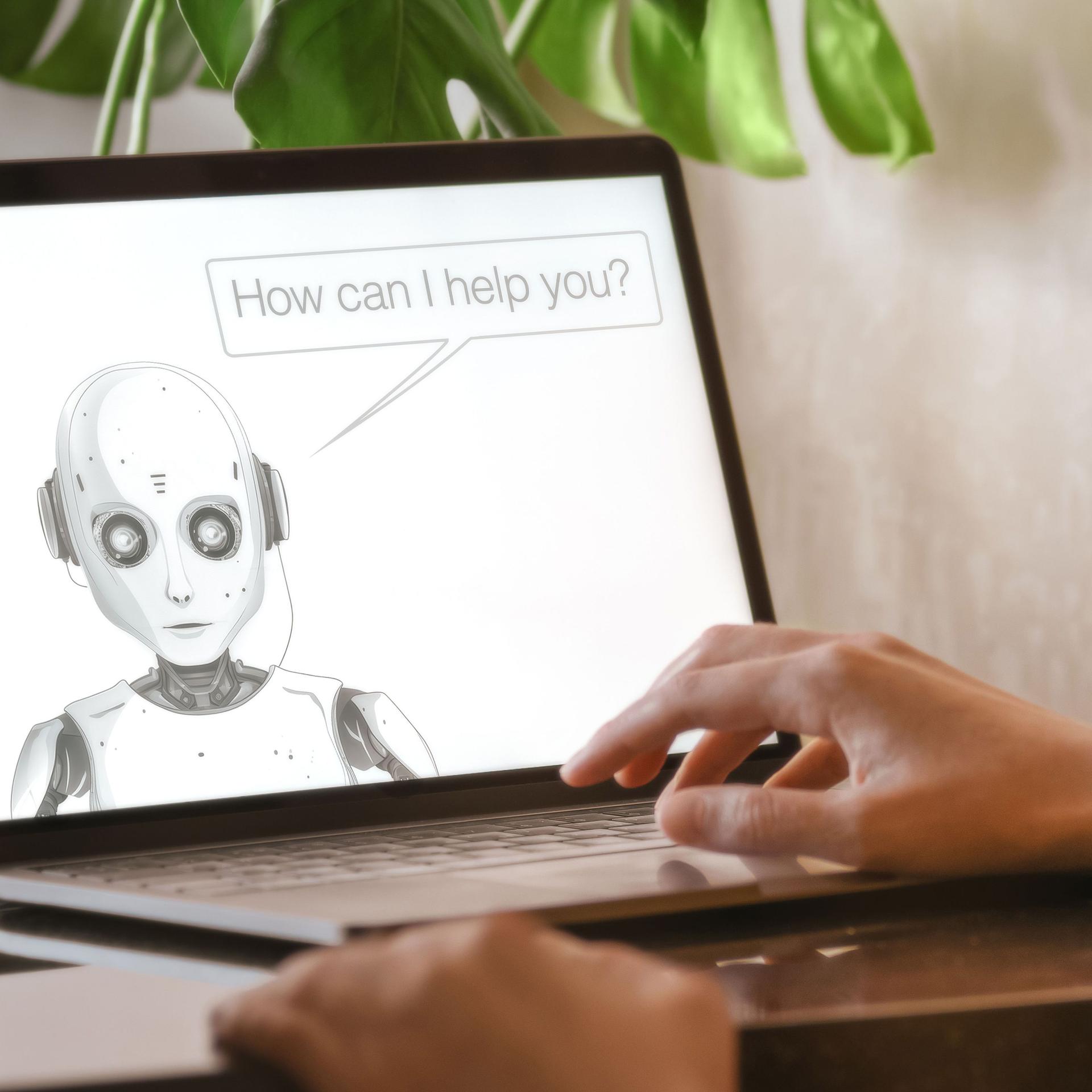 Hand auf einem aufgeklappten Laptop, auf dem Bildschirm ist ein gezeichneter Roboter, der mit der Person redet.