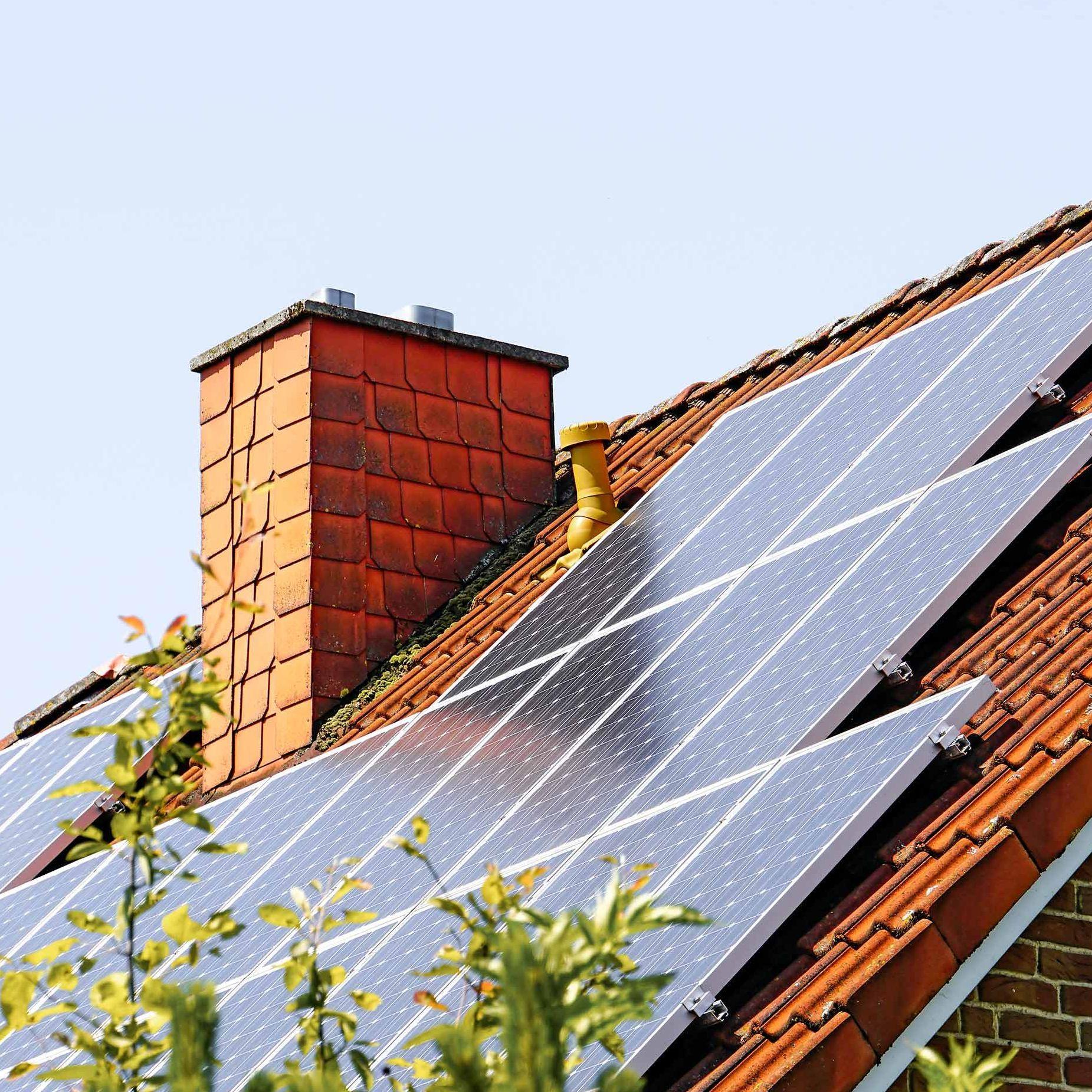 Von einem Einfamilienhaus ist nur das Dach und ein Schornstein zu sehen. Auf der Dachschräge sind eine Vielzahl von Solarpannels zu sehen.