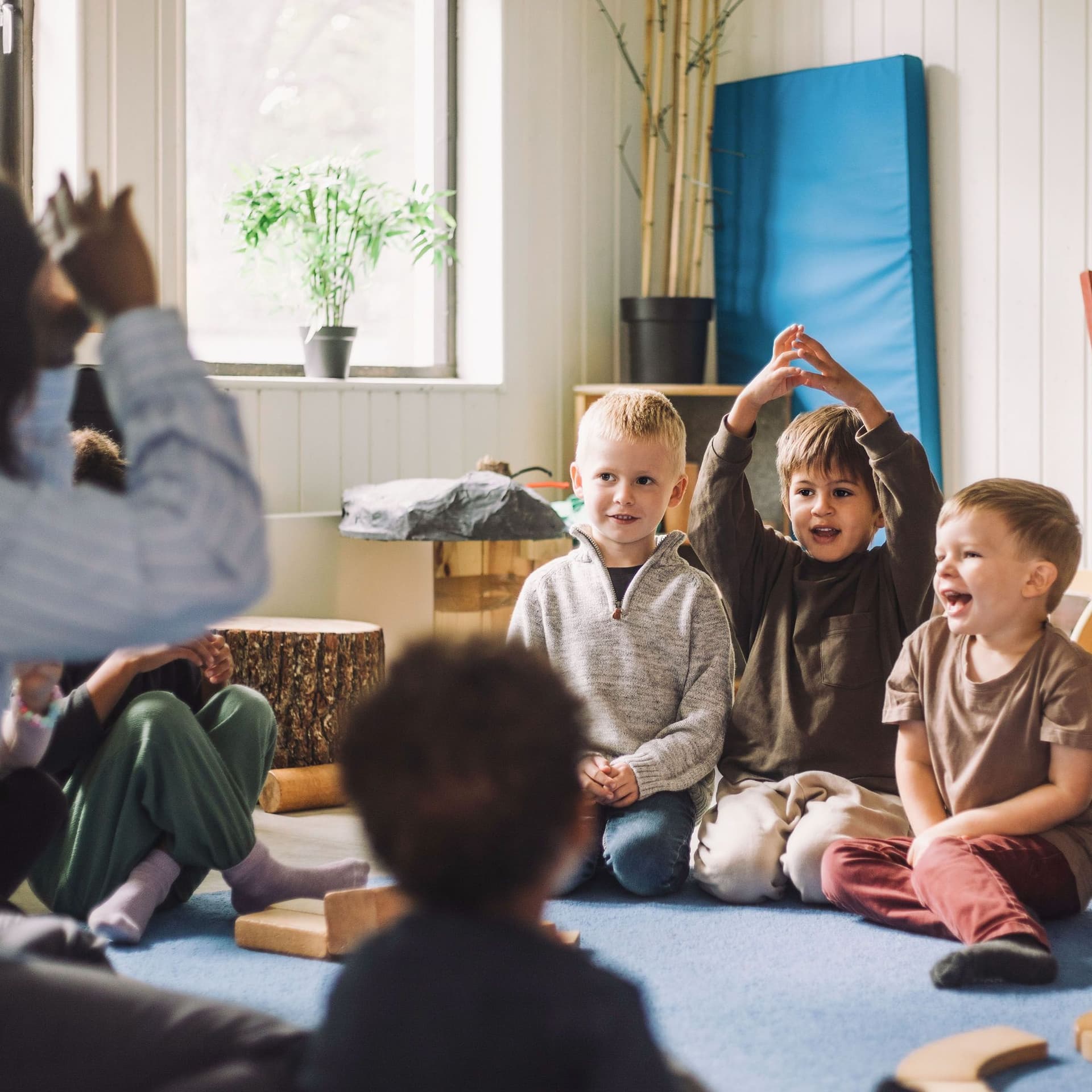 Eine Erzieherin sitzt in einer Kindertagesstaette mit einer Kindergruppe in einem Sitzkreis.
