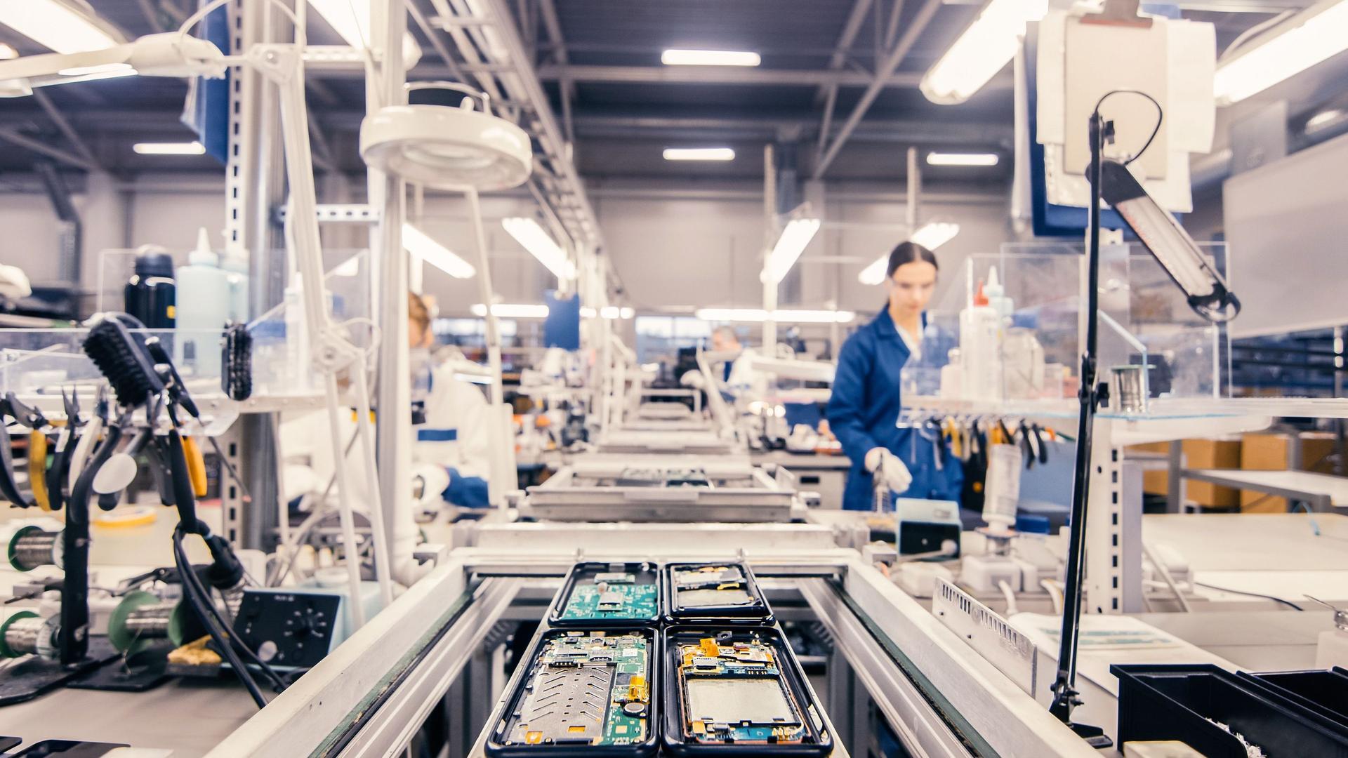 Frau in blauer Arbeitskleidung in einer Fabrik, die am Fließband arbeitet.