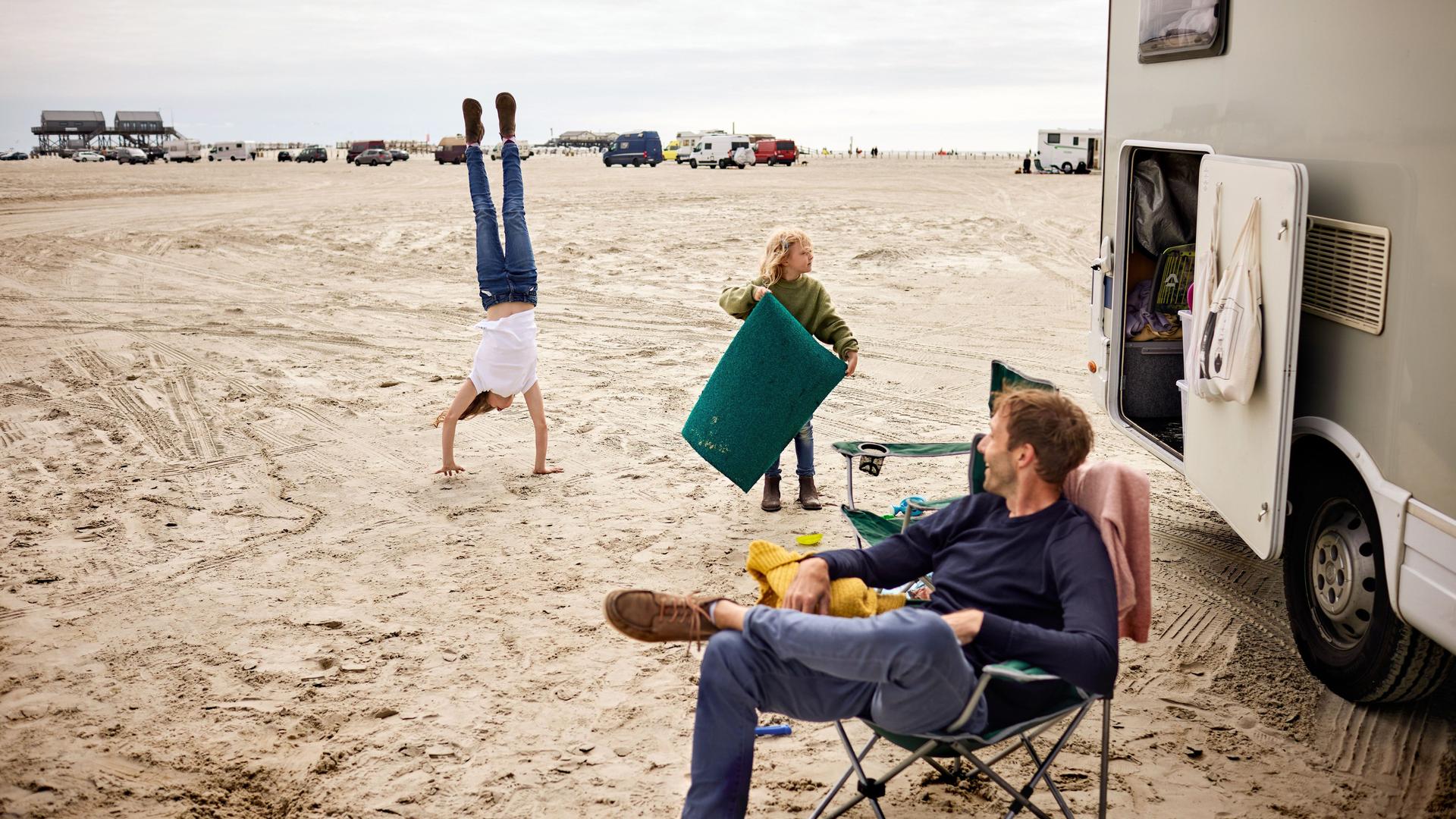 Vater spielt mit seinen zwei Kindern vor Wohnwagen am Strand
