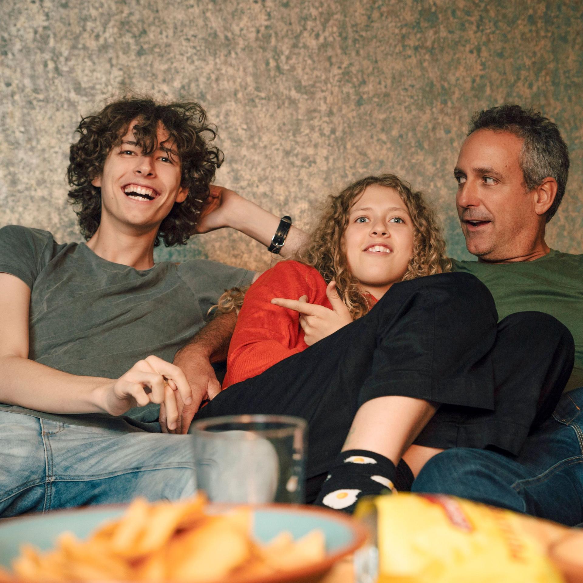 Fröhliche Familie auf dem Sofa beim Fernsehen mit Chips