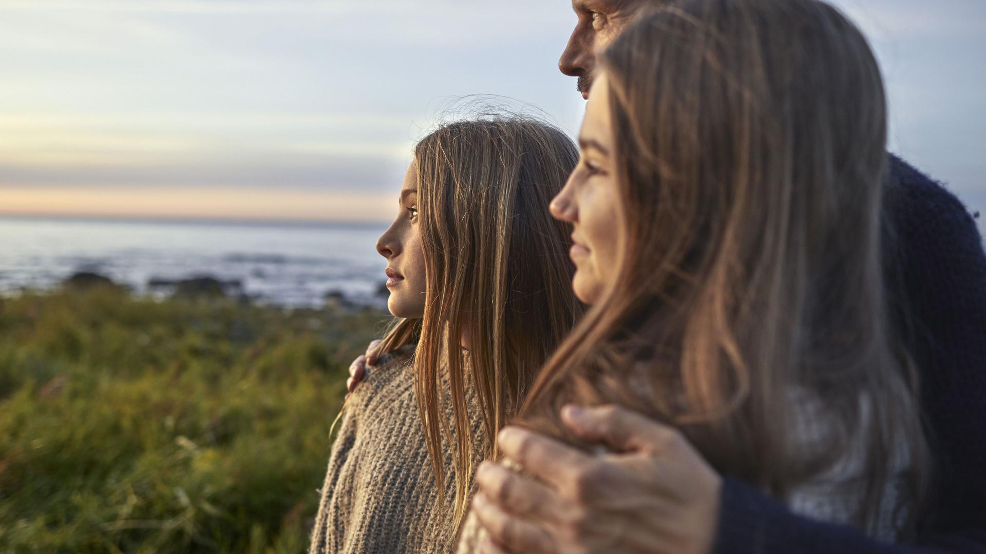 Vater blickt mit seinen zwei Töchtern auf das Meer