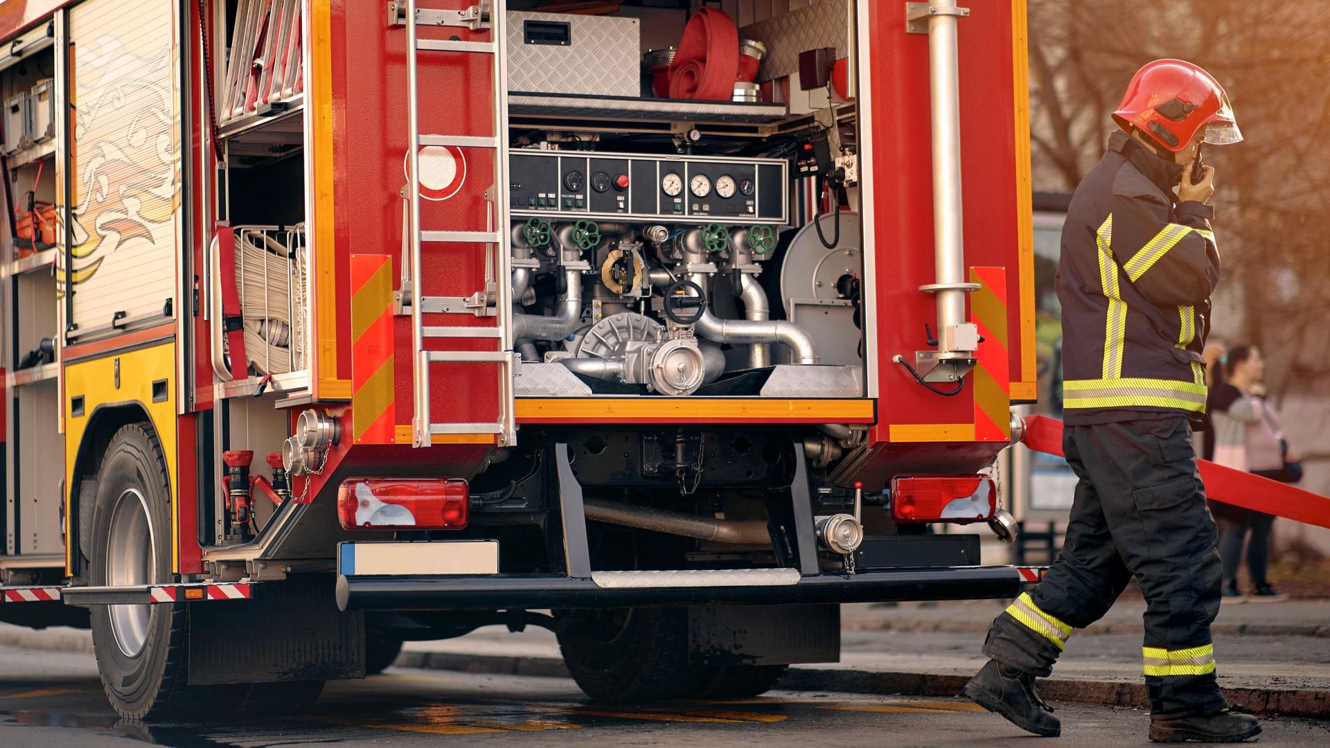 Rotes Feuerwehrfahrzeug mit Feuerwehrmann im Vordergrund im Einsatz.