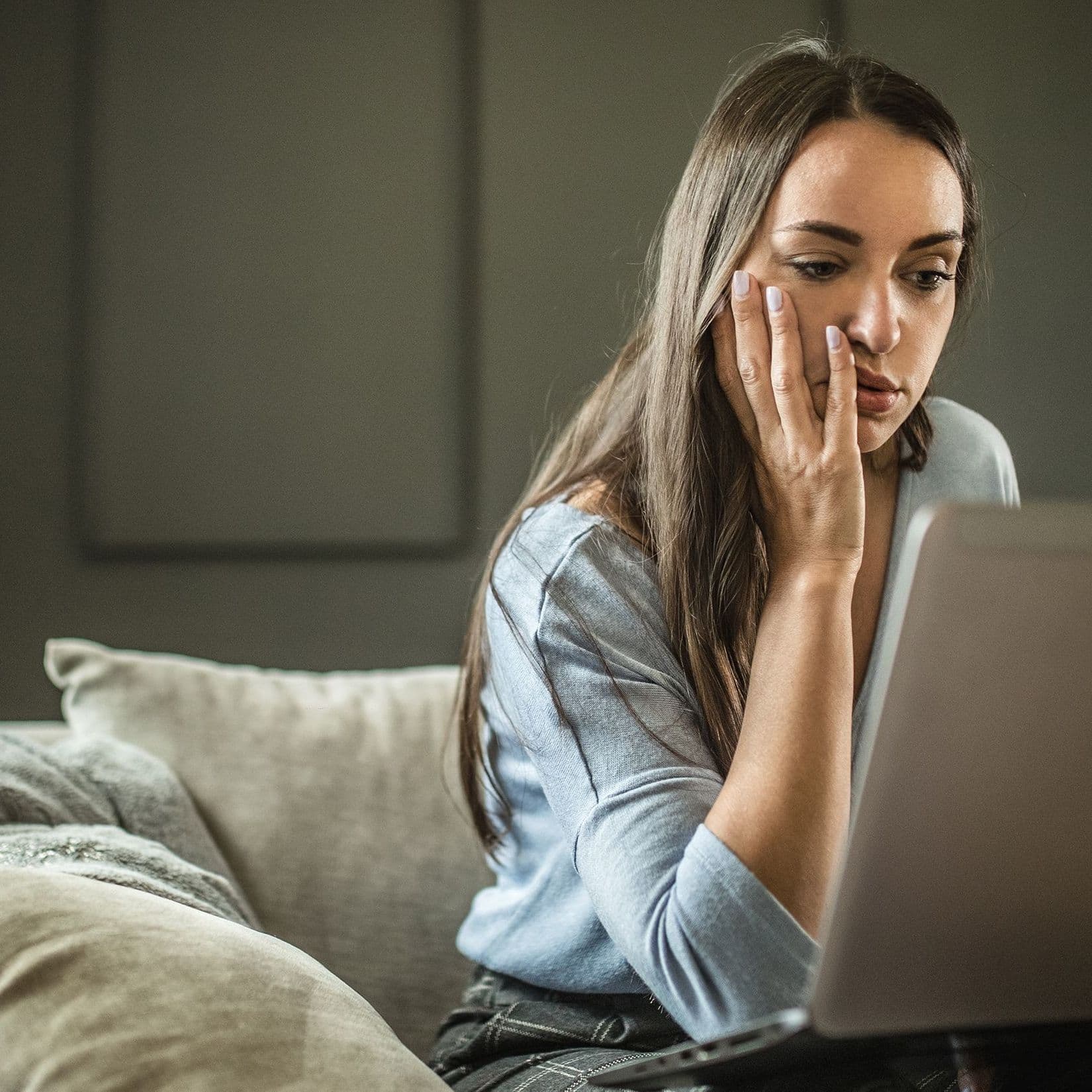 Frau auf Sofa mit Laptop besorgt