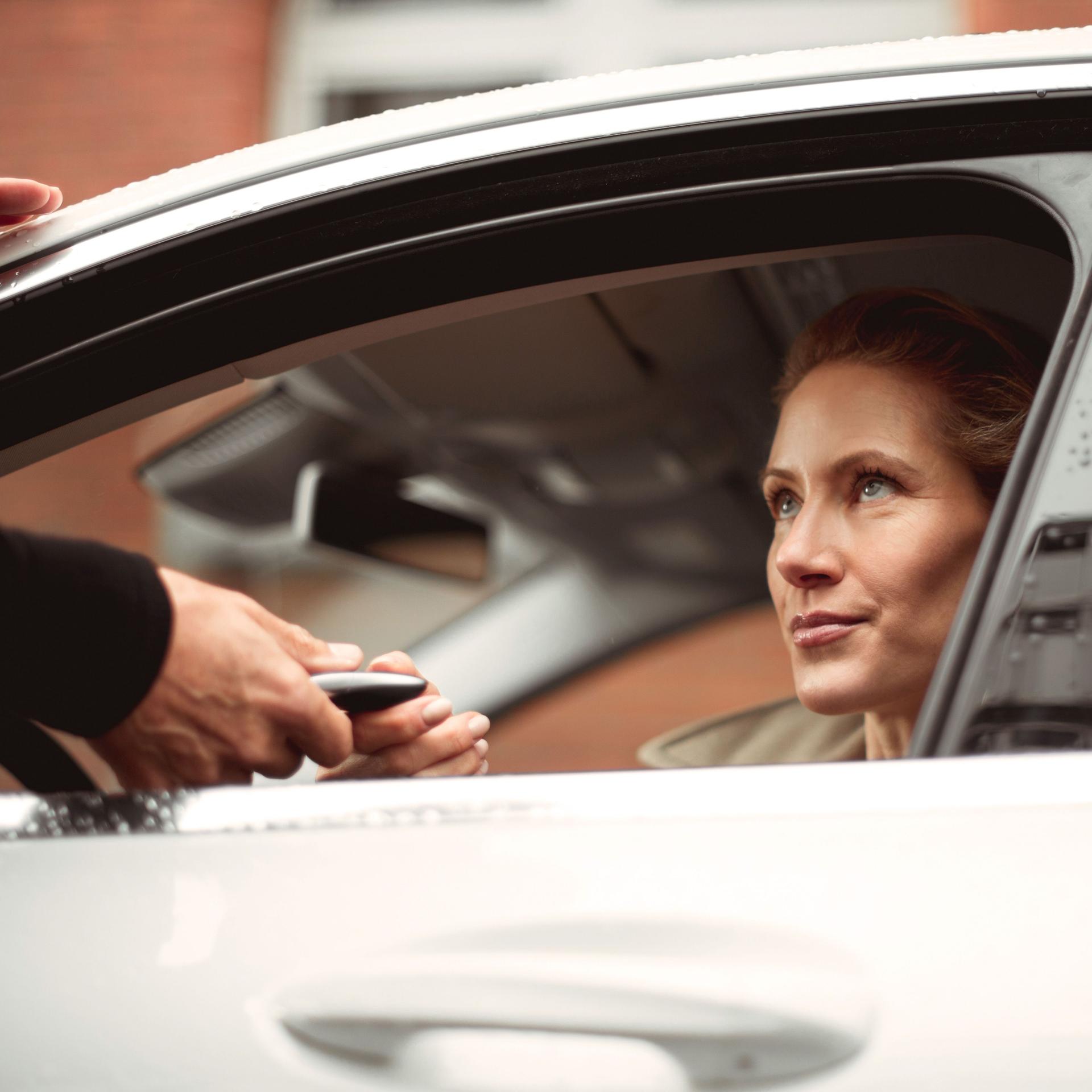 Eine Frau sitzt am Steuer einen Autos und erhält durch das offene Fahrerfenster den Autoschlüssel.