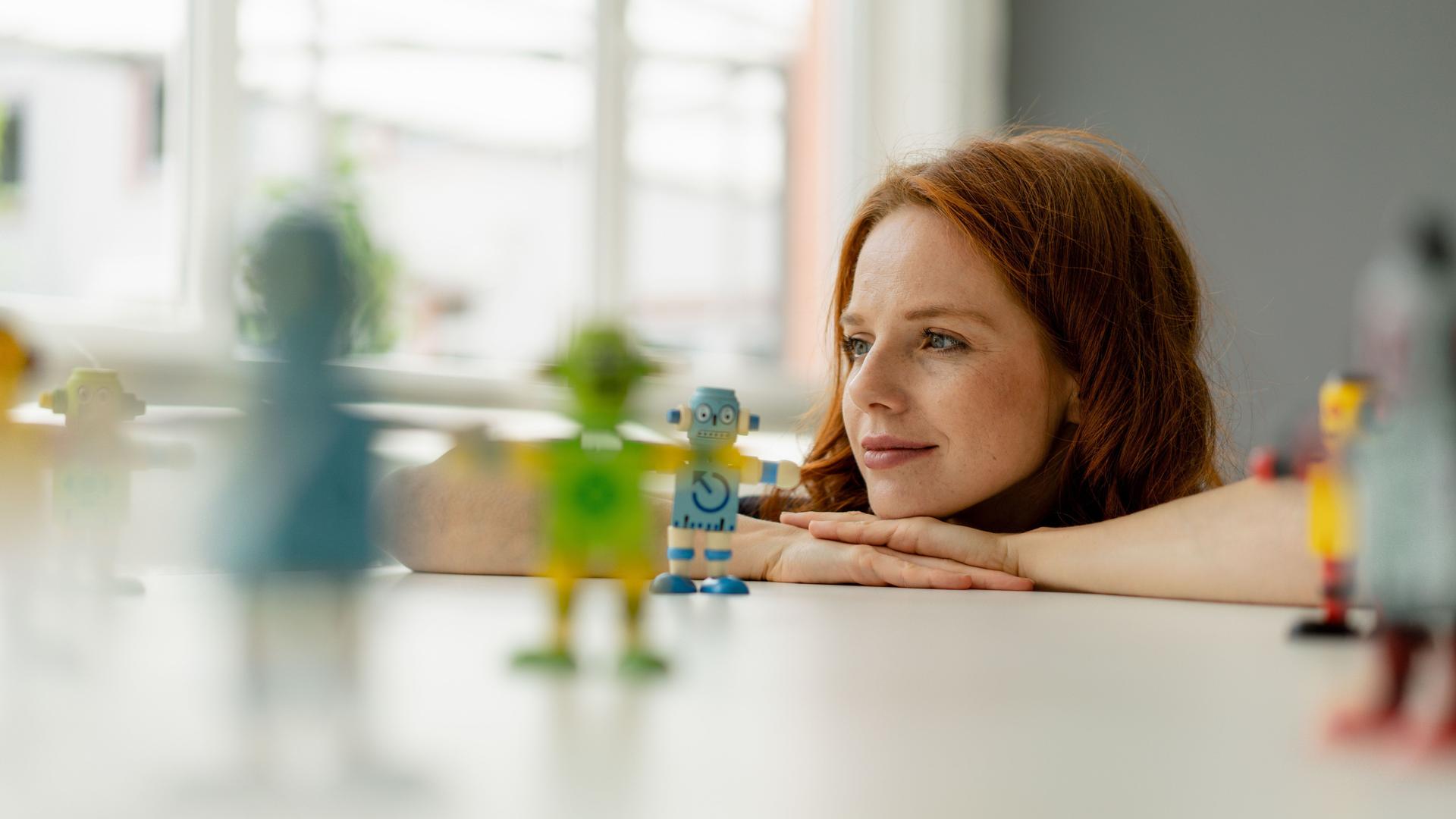 Porträt einer jungen Frau, die sich Miniaturroboter aus Holz auf einer Tischplatte.ansieht.