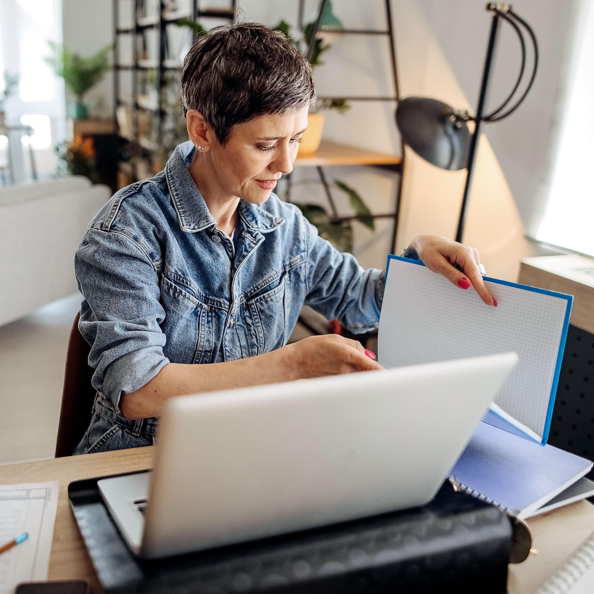 Aufnahme einer jungen Frau, die einen Laptop benutzt und Papierkram durchgeht, während sie von zu Hause aus arbeitet