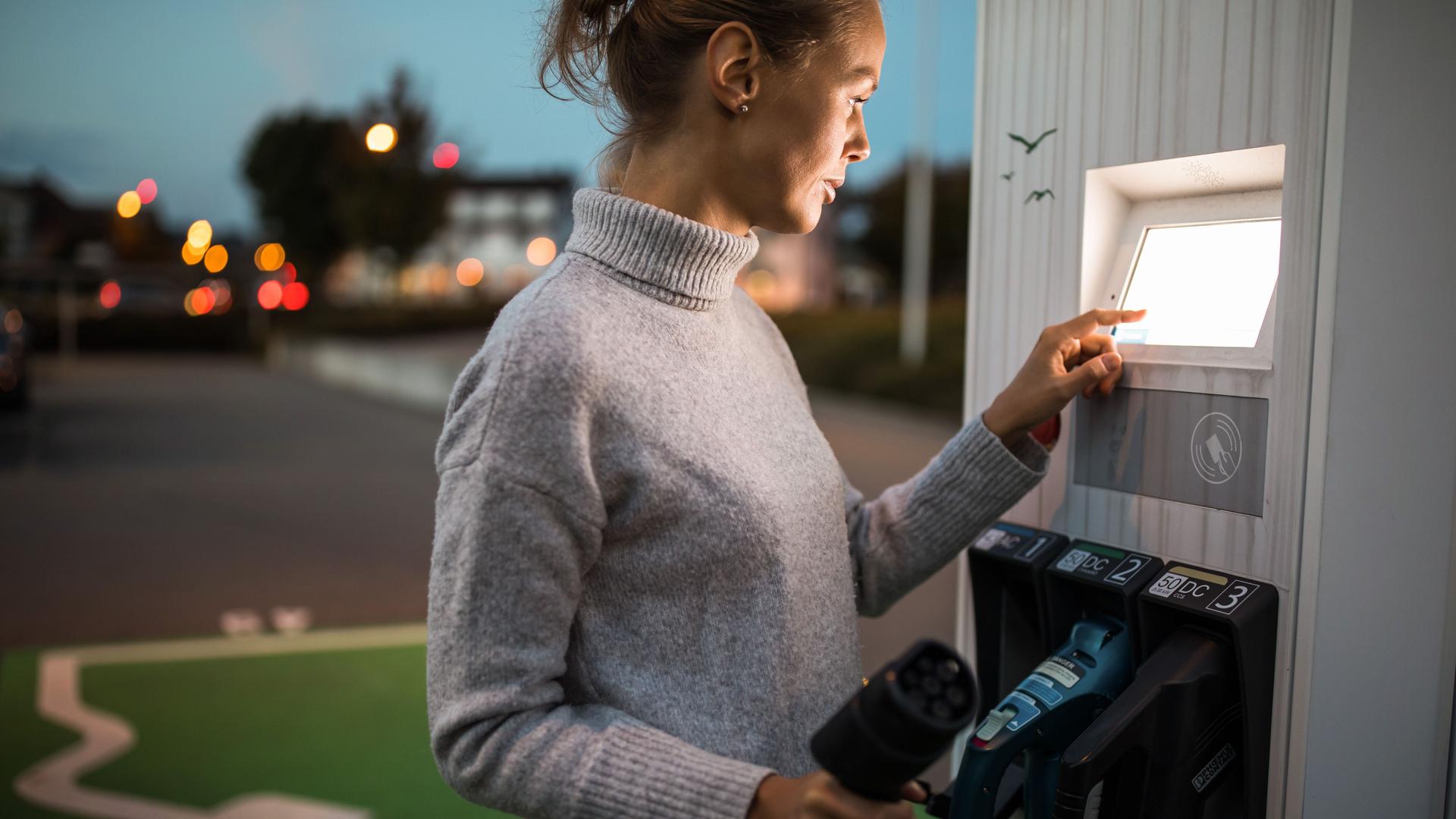 Ein junge Frau bezahlt an einer Ladesäule für Elektroautos.