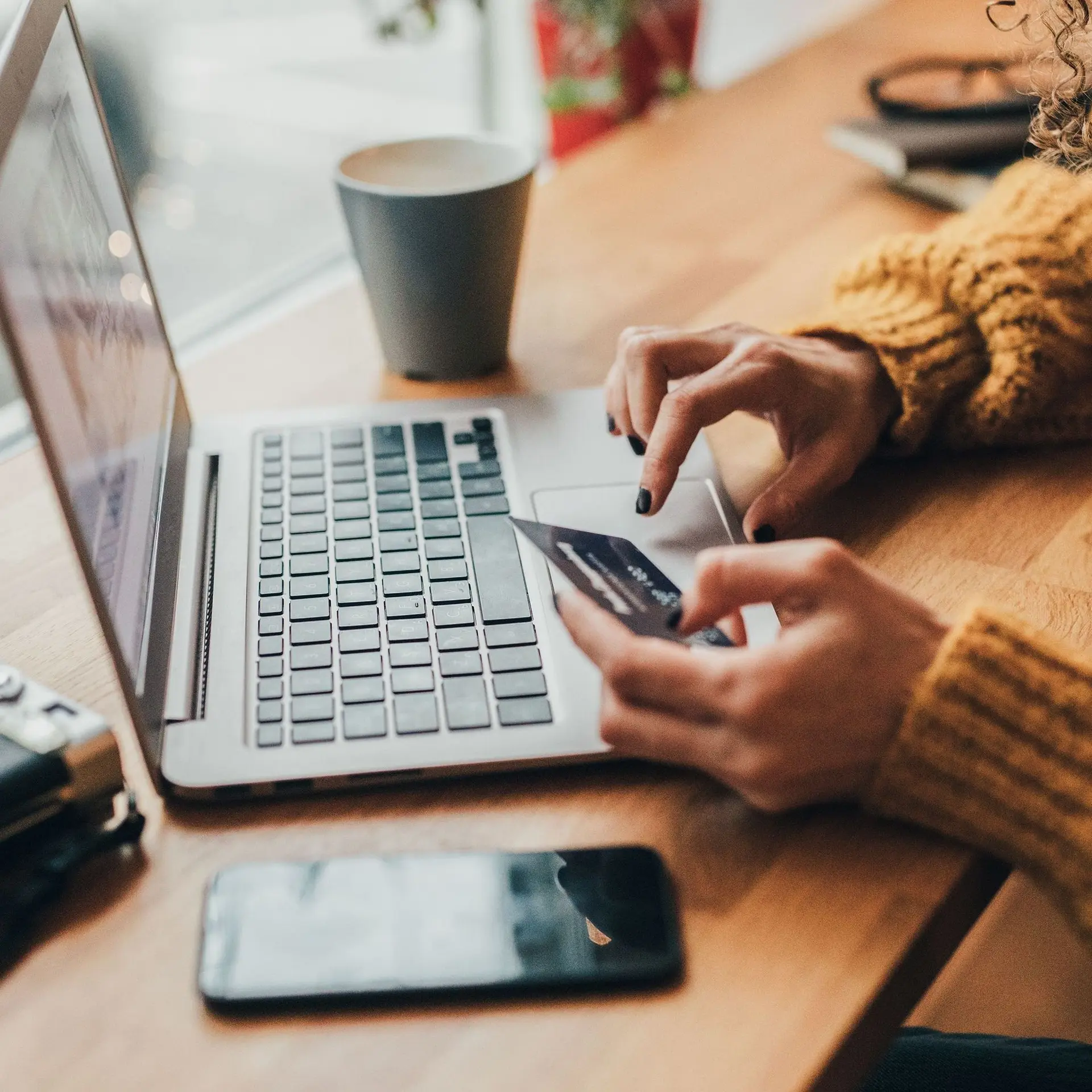 Nahaufnahme von den Händen einer Frau, die eine Bankkarte in der Hand hält und auf der Tastatur eines Laptops tippt.