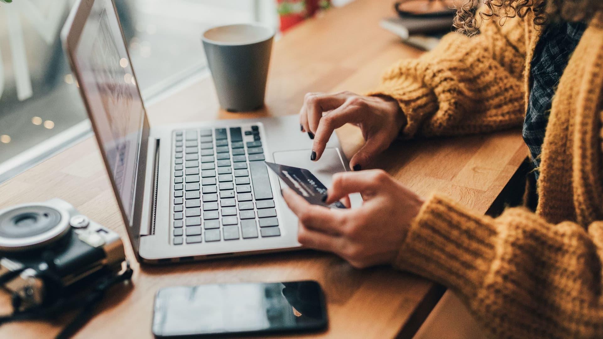 Nahaufnahme von den Händen einer Frau, die eine Bankkarte in der Hand hält und auf der Tastatur eines Laptops tippt.