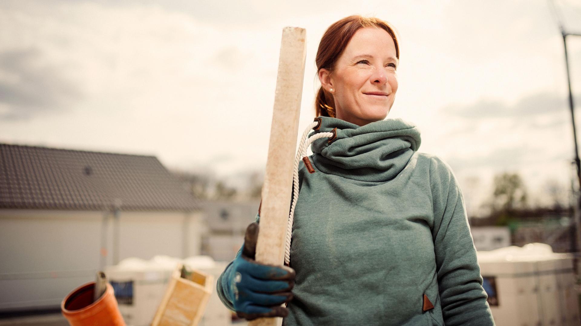 Eine Frau steht mit einem Stück Holz in der Hand auf einer Baustelle.