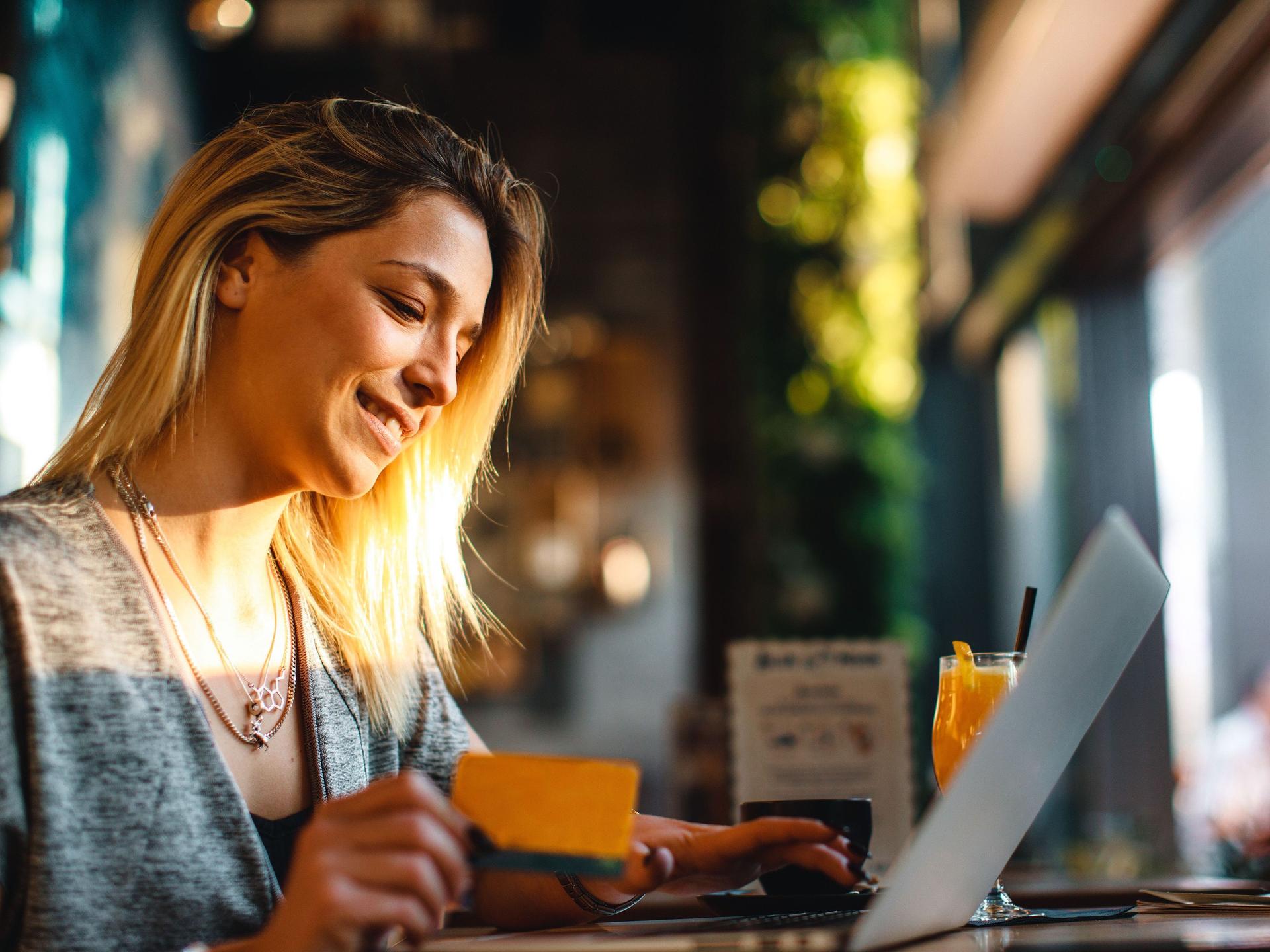 Frau in einen Cafe mit Laptop und Kreditkarte in der Hand.